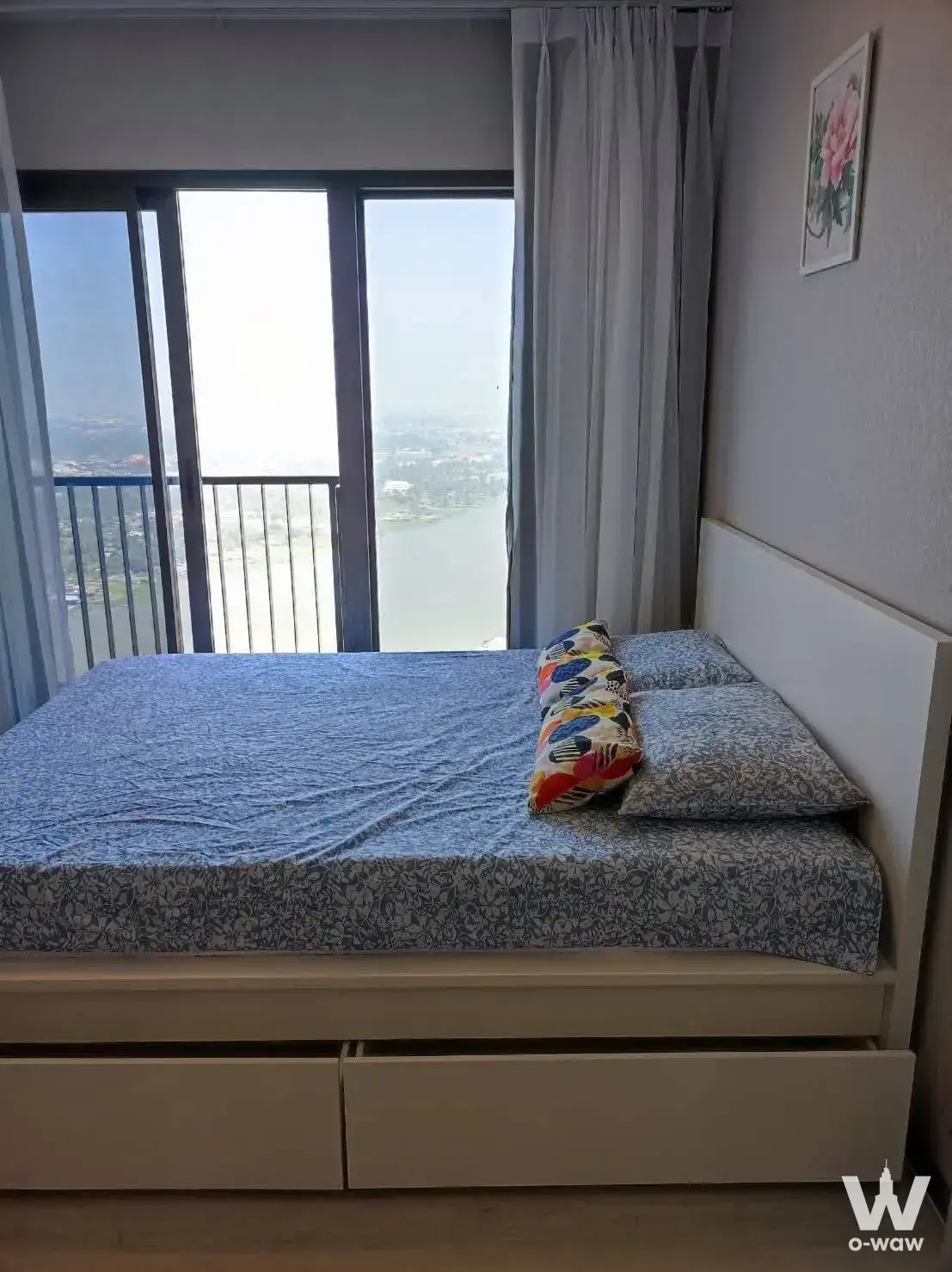 1-bed condo for rent in The Politan Aqua bedroom with river views, blue-grey floral bedding, and light wood laminate flooring
