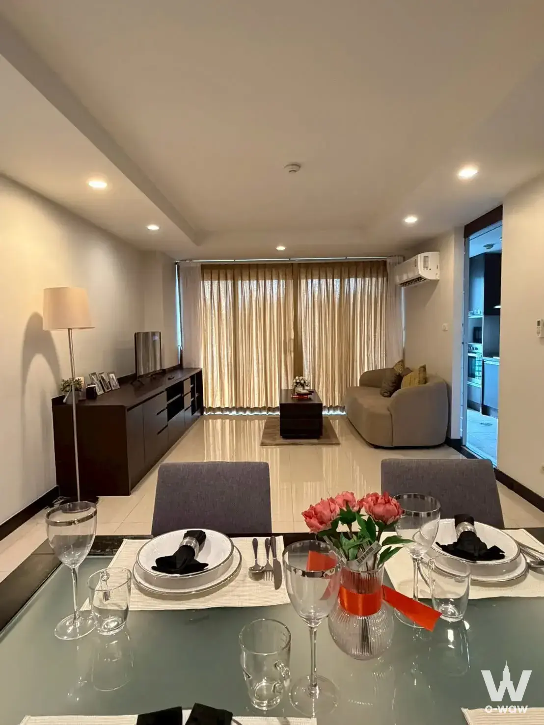 Dining and living area in The Avenue Sukumvit 61 condo with glass table, pink roses, and beige sofa