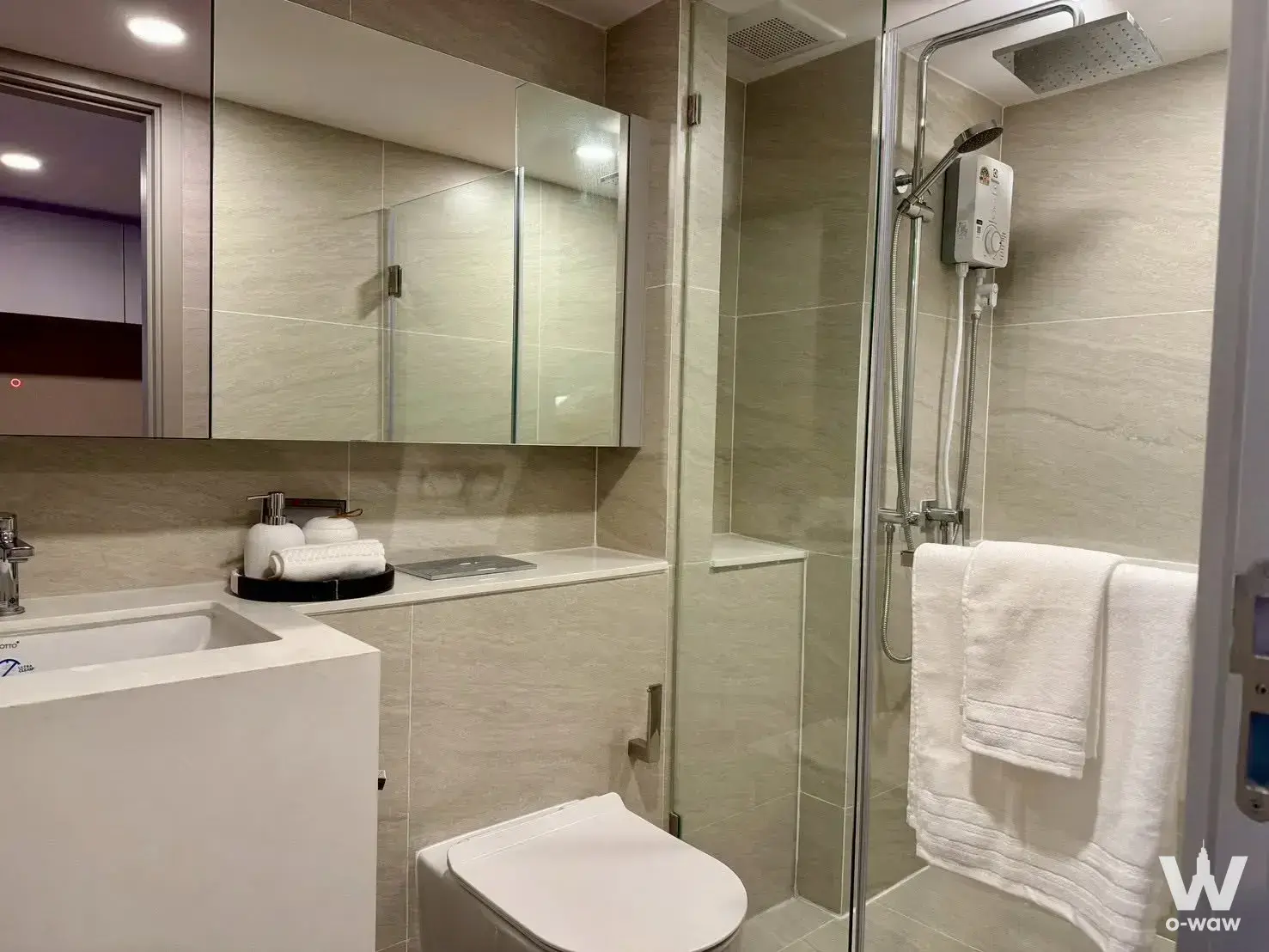 Modern bathroom with beige stone tiles and glass shower enclosure in a So Origin Kaset Interchange 1-bed condo for sale