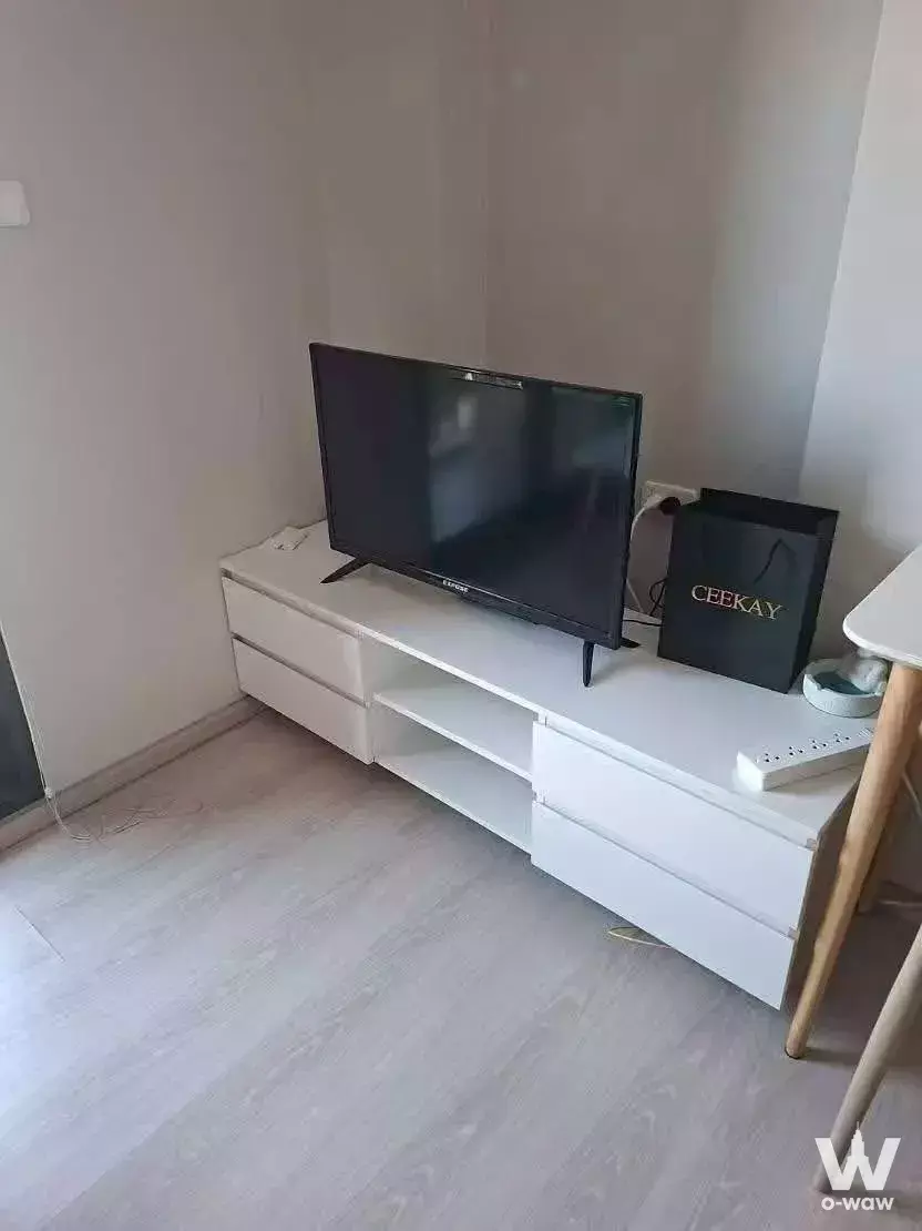 Minimal living room in a 1-bed NUE Noble Srinakarin condo featuring a white TV console and black flat-screen