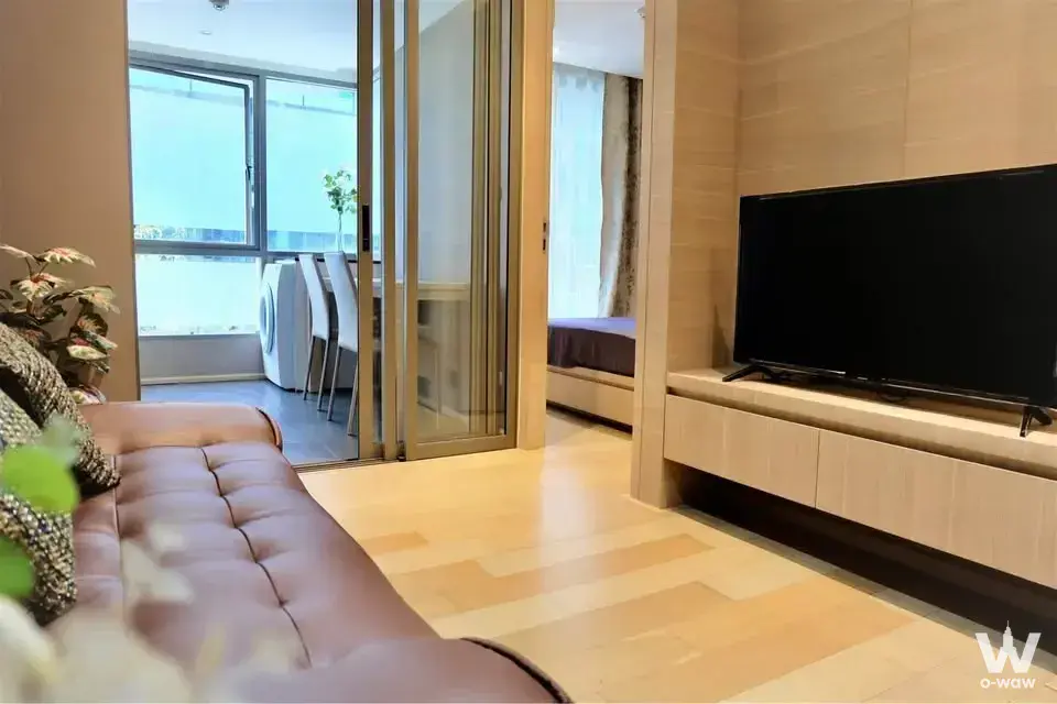 1-bed condo for rent in Klass Silom Condo living room with brown leather sofa and gold-framed partition doors