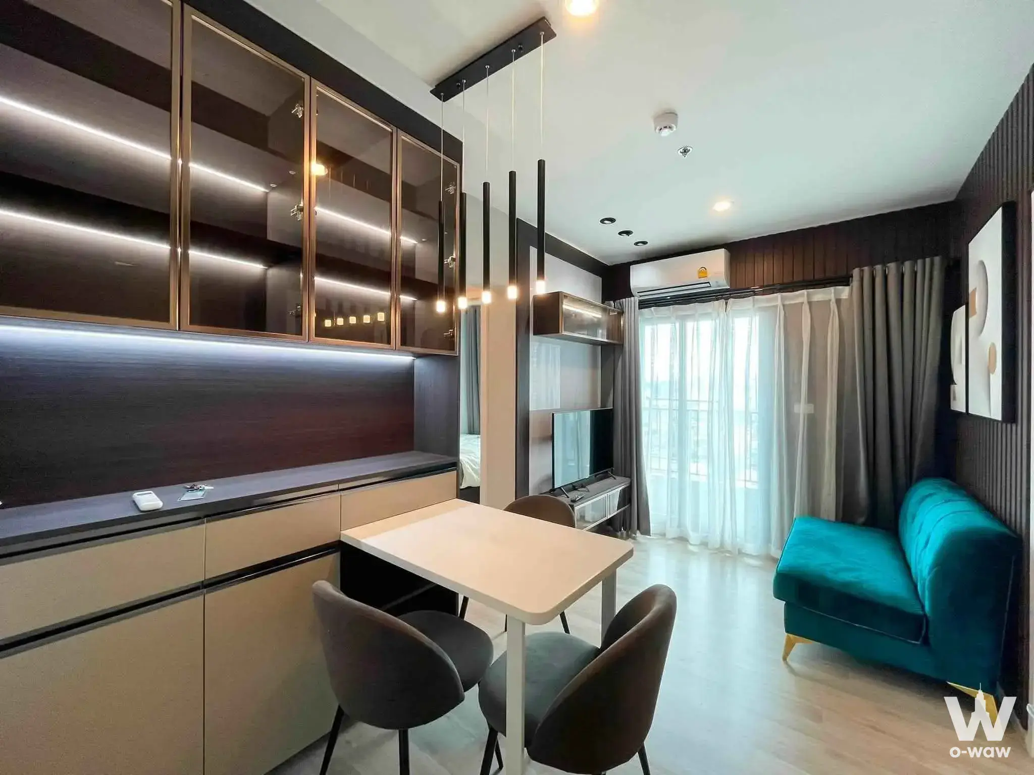 The Privacy Rama 9 open-plan condo with teal velvet sofa, dark wood cabinetry, and modern dining area