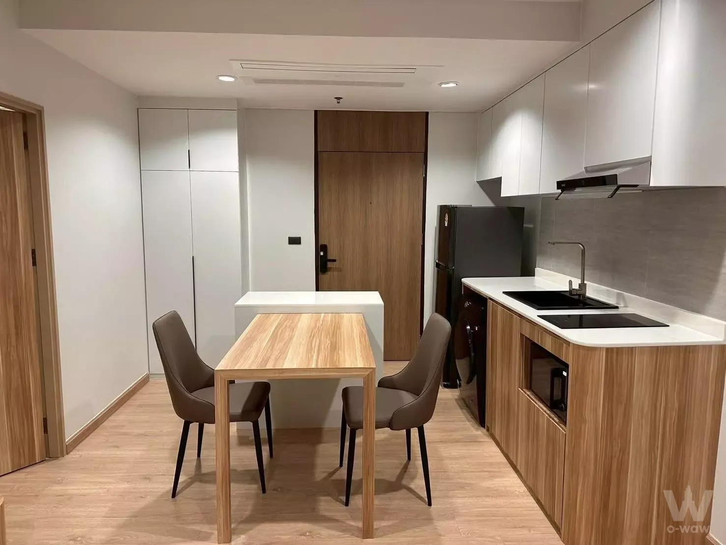 Open-plan dining area in a 1-bed Noble Remix condo with oak table and modern galley kitchen