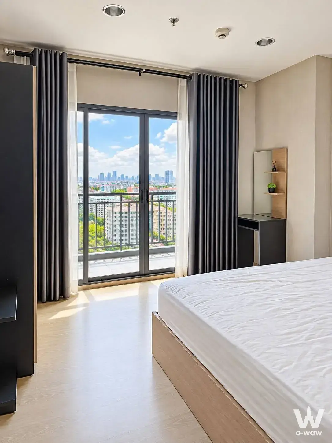 Master bedroom in a 2-bed condo rental at IDEO Sukhumvit 115 has a low wooden bed and a sliding door to a city-view balcony
