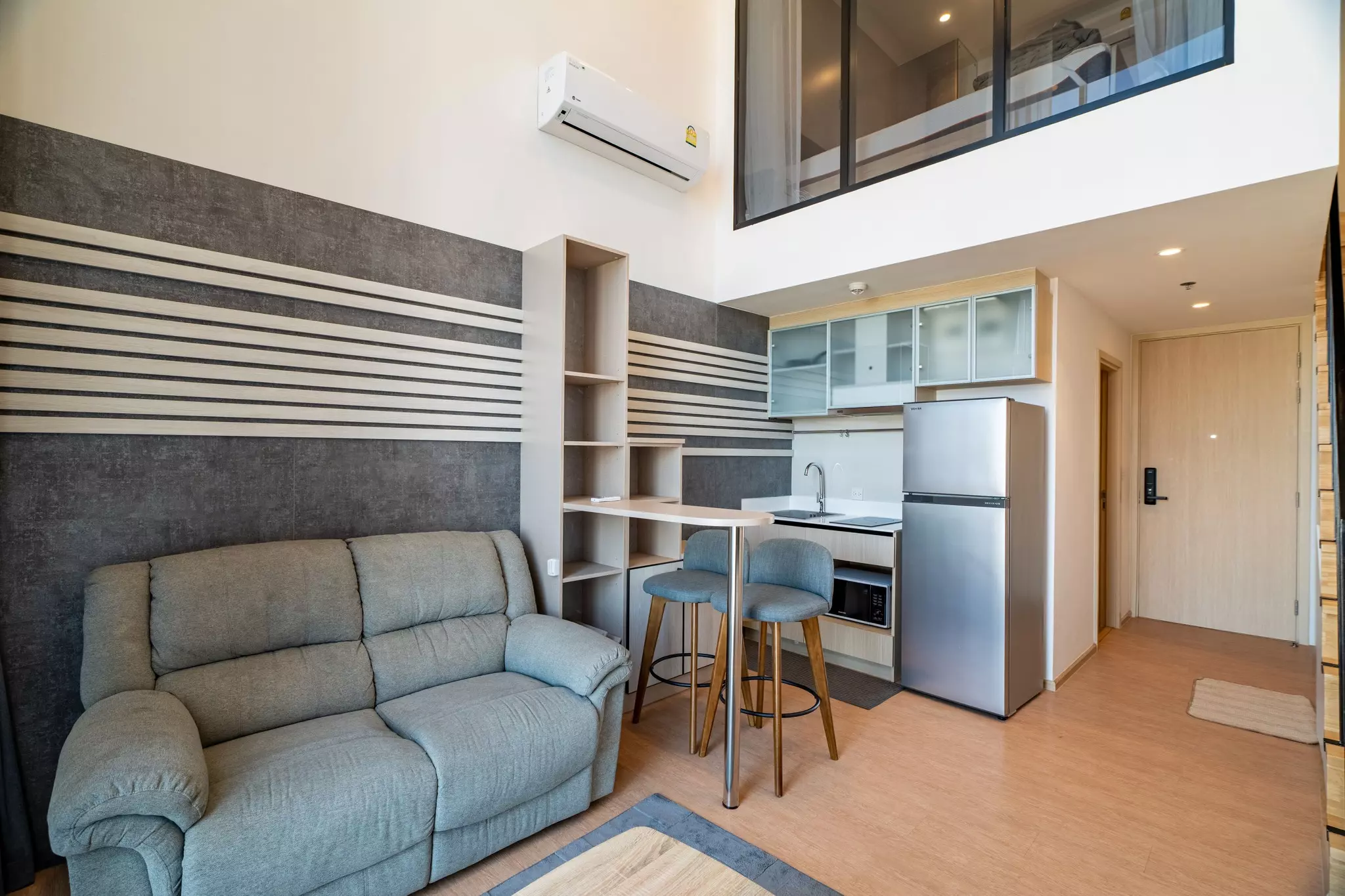 Duplex loft living room with grey concrete accent wall and mezzanine bedroom view in MARU Ekkamai 2