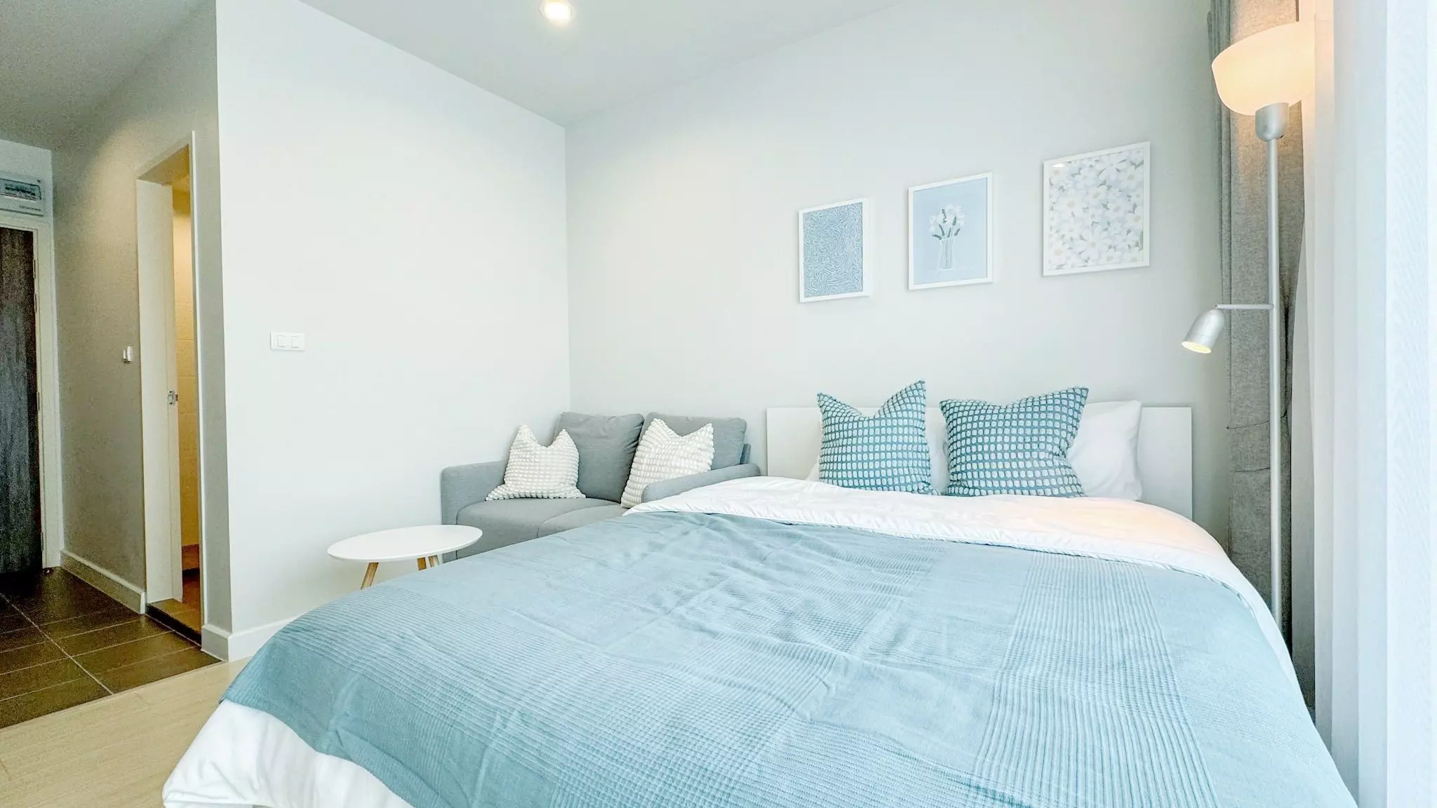 Queen bed with blue duvet and grey sofa in this 1-bed rental at Metro Sky Wutthakat