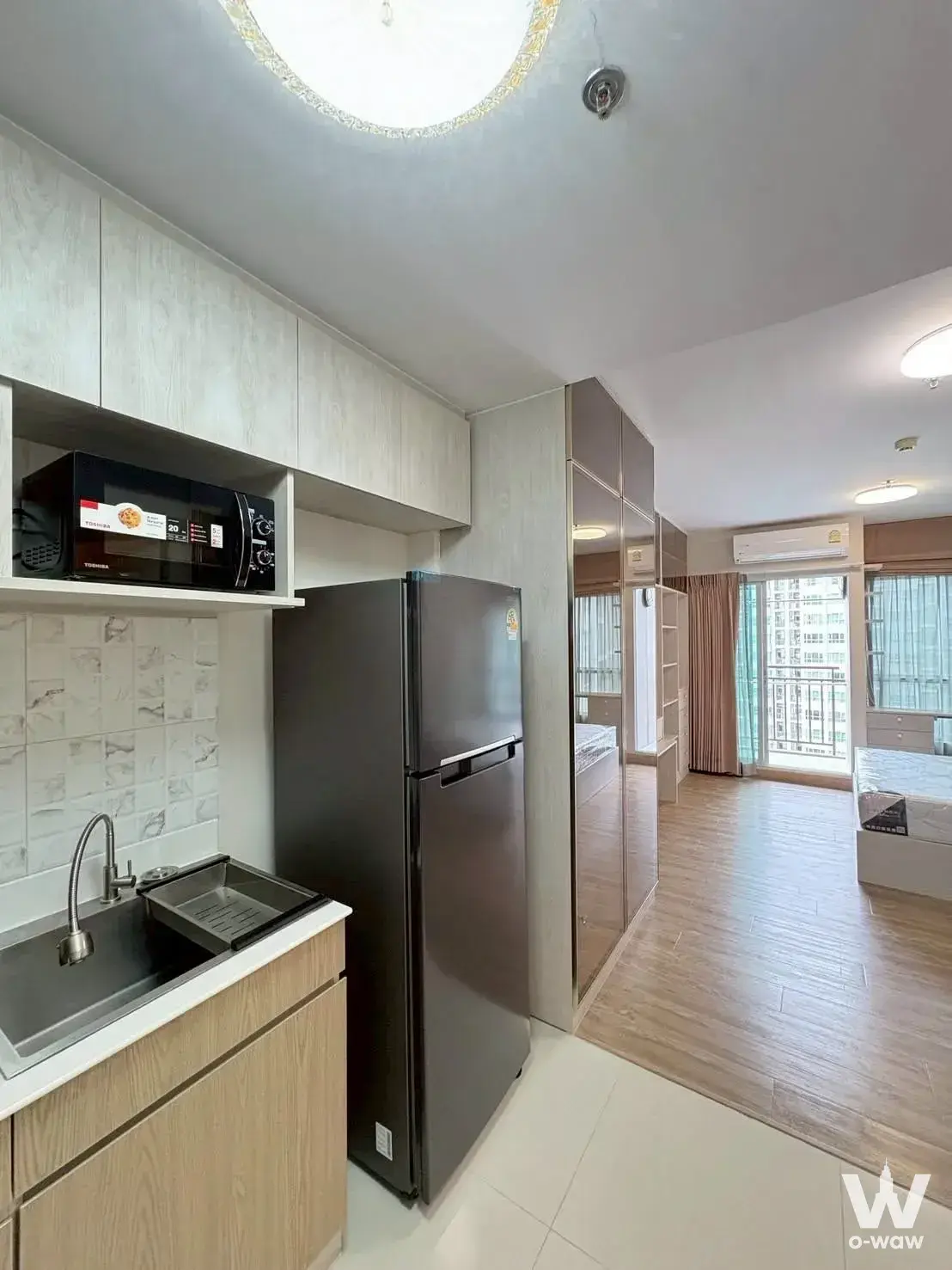 Open-plan studio in Supalai Veranda Rama 9 with light wood cabinets and a mirrored wardrobe