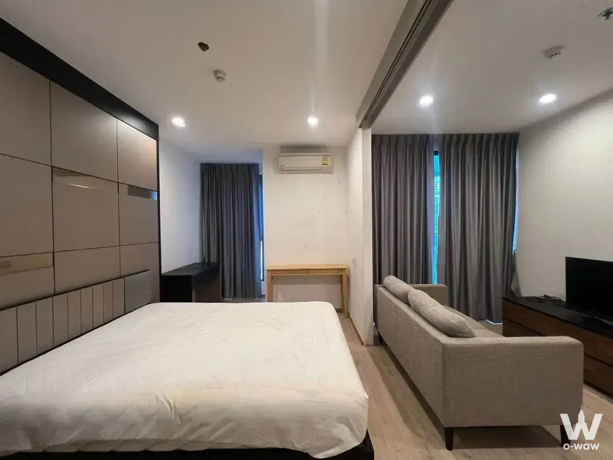 Studio bedroom in an Ideo Q condo with a queen bed against taupe panels and floor-to-ceiling grey curtains