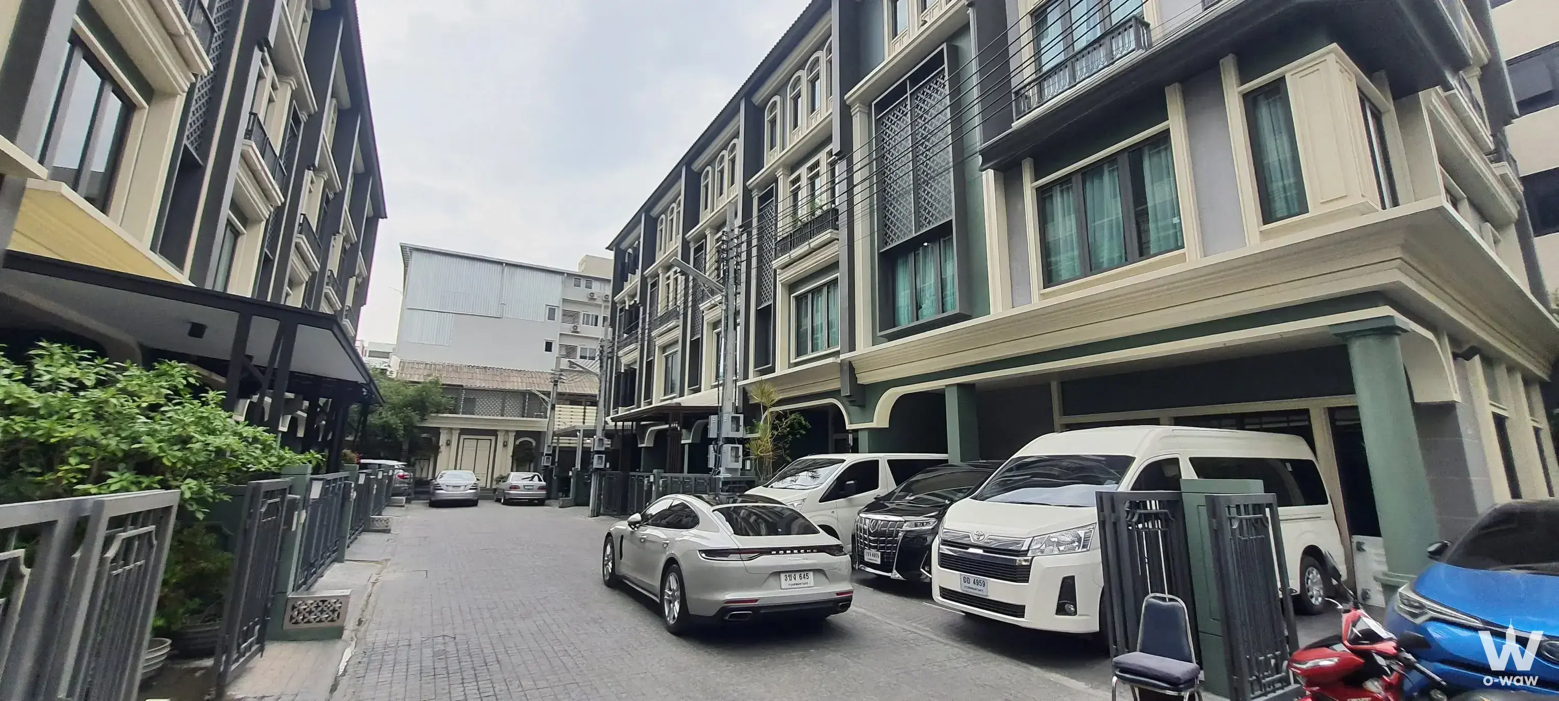 Street view of Tiger Lane Sansiri townhouses with dark facades and a silver Porsche parked on the brick driveway