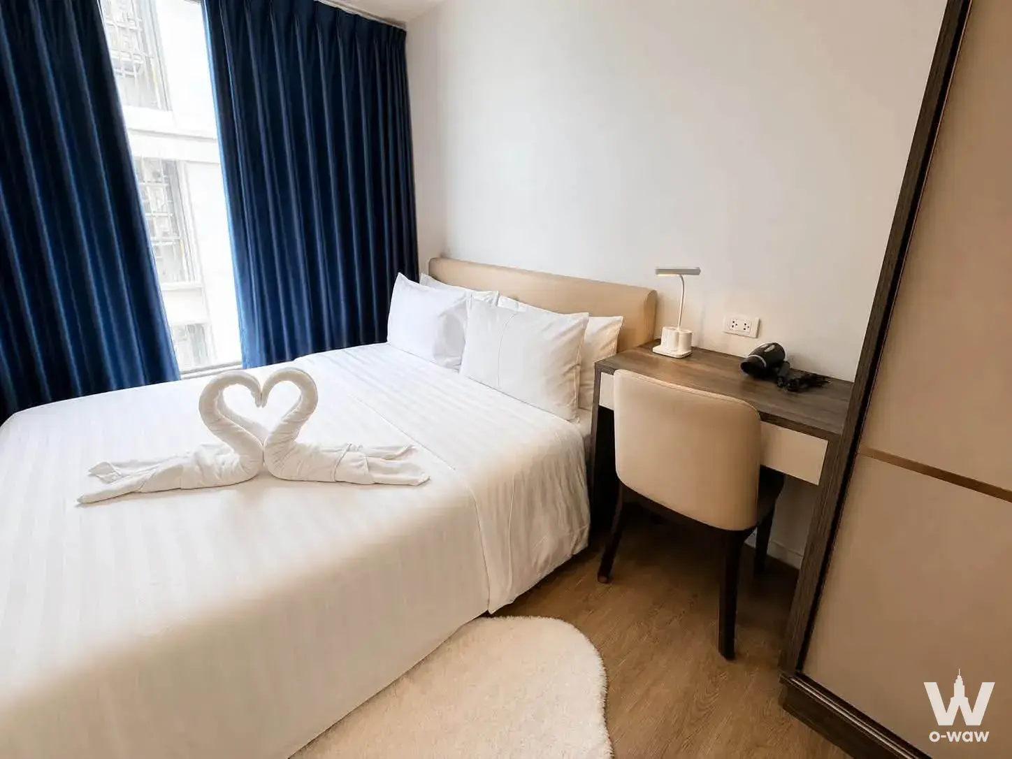Modern bedroom in The Nest Sukhumvit 64 with beige linens, navy drapes, and a compact desk area