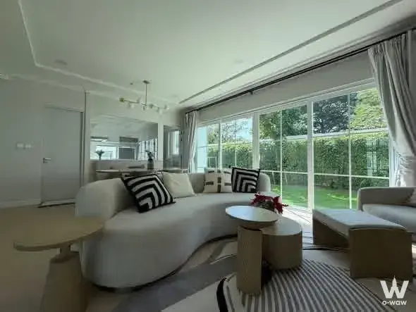 Living room of a 4-bed house for rent in Chaiyapruek Bangna KM.15 features a curved white sofa and garden-view sliding doors