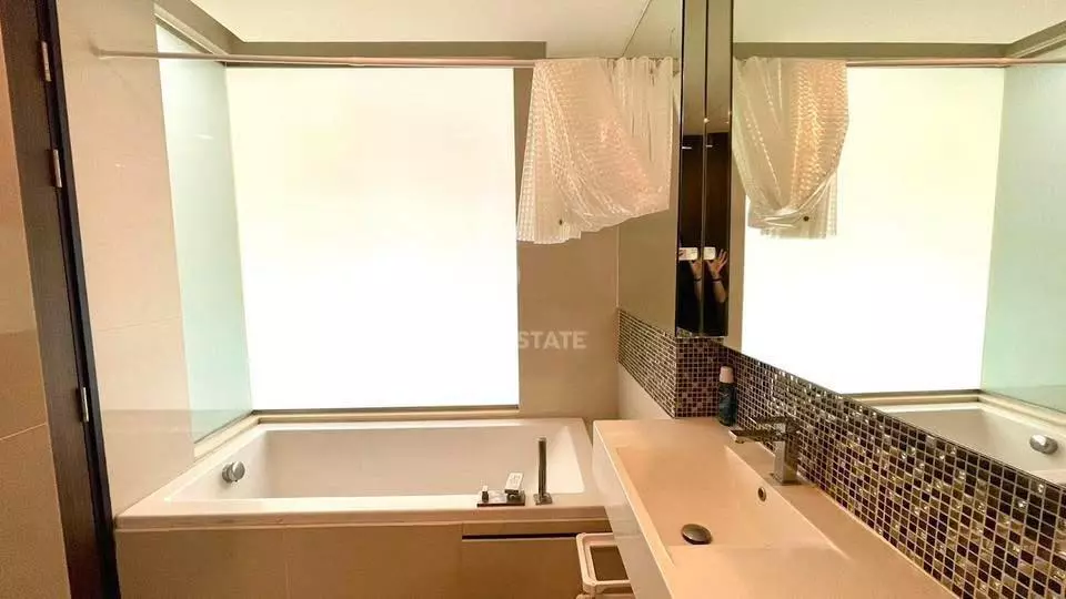 Spacious bathroom in a RHYTHM Sukhumvit 44/1 condo featuring a white soaking tub and long vanity with dark mosaic tile