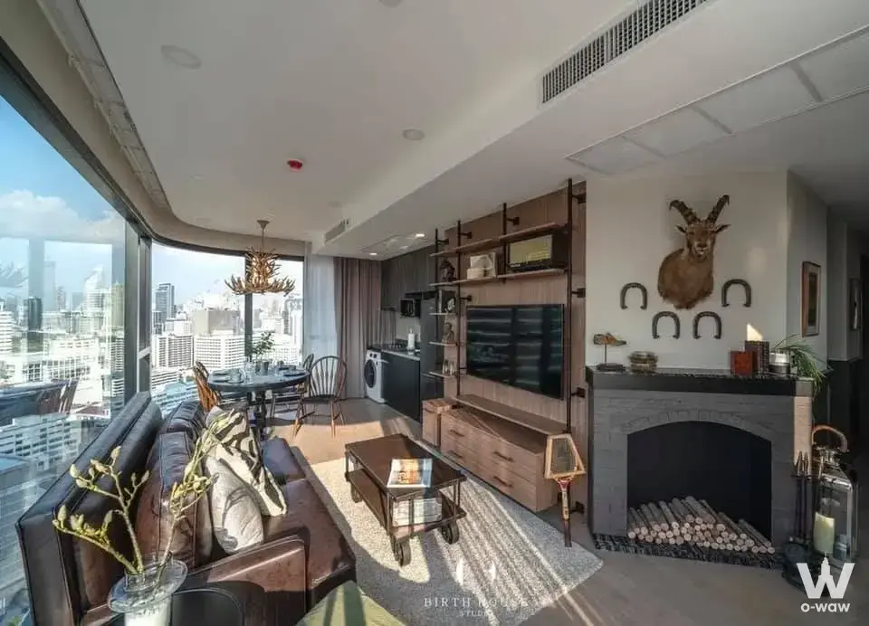 Luxury loft living area with dark leather sectional, brick fireplace, and city views in Ashton Chula-Silom