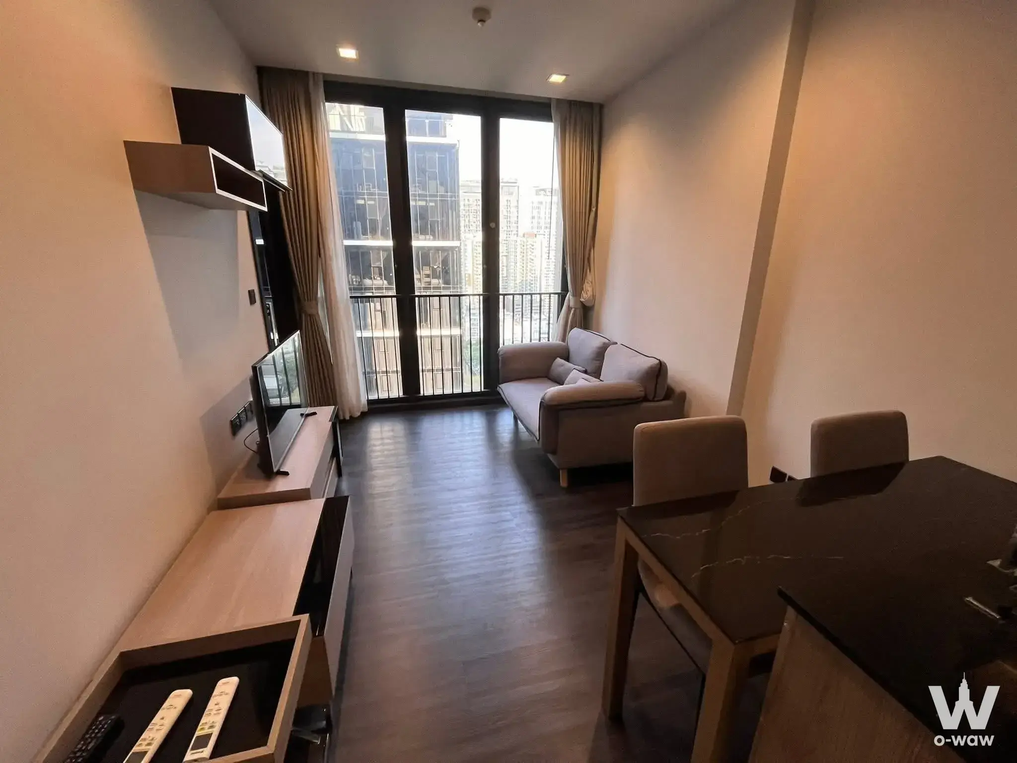 Living room with grey sofa and dining set near sliding glass doors in a 1-bed condo for rent at THE LINE Asoke-Ratchada