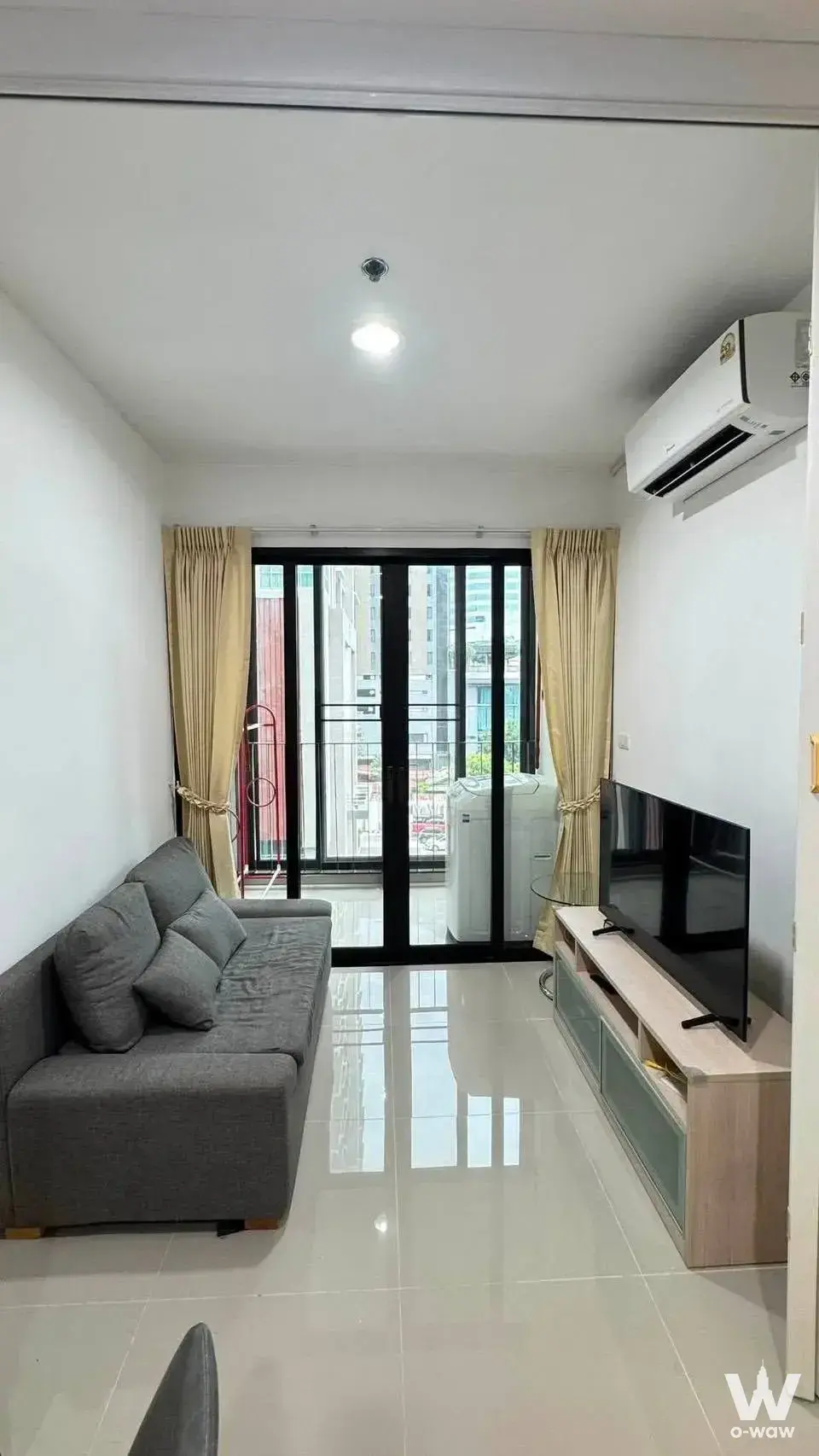 Grey sofa and glass balcony door in a furnished 1-bed condo for rent at IDEO Ratchada-Huai Khwang