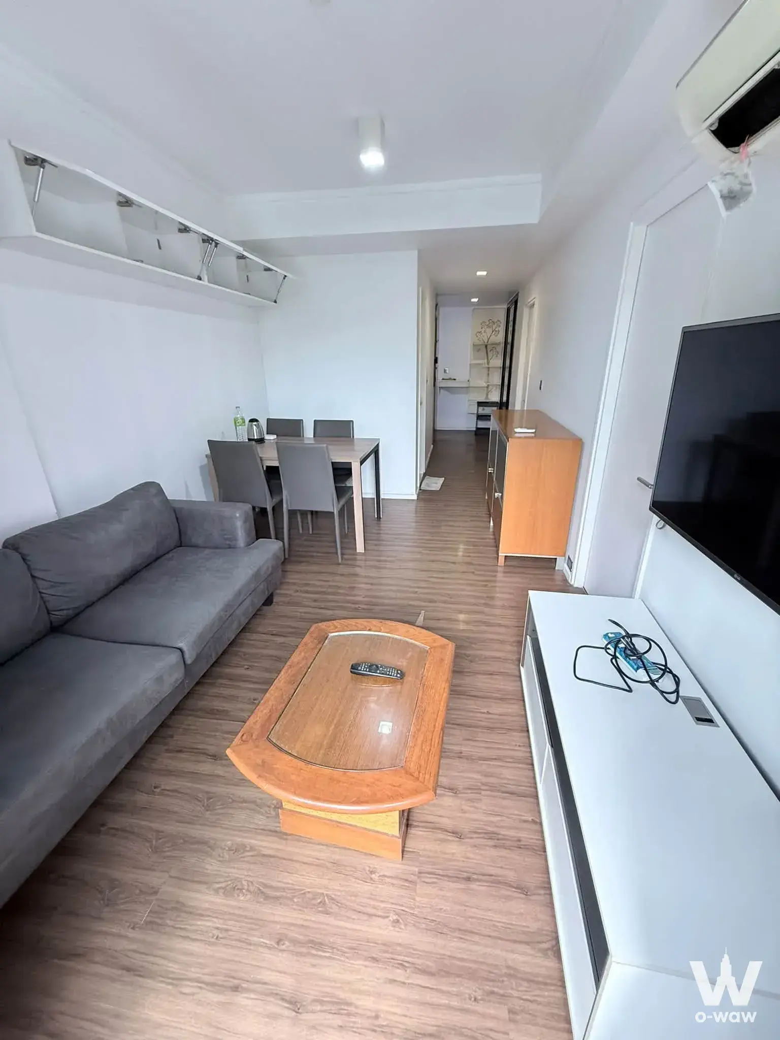 Open-plan living and dining area in a Than Living Ratchada condo featuring grey sofa and wood accents