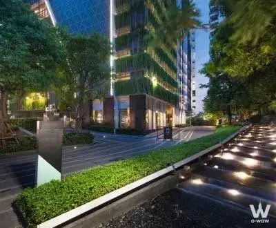 Ideo Q Ratchathewi 1-bed exterior at dusk with glass facade, LED strips, and landscaped courtyard