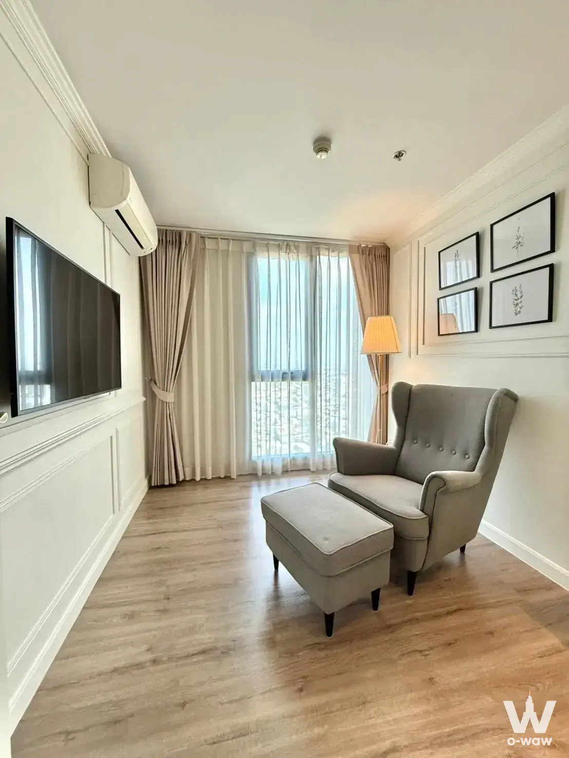 Living room corner in C Ekkamai Condominium with a grey wingback chair, wall-mounted TV, and city view