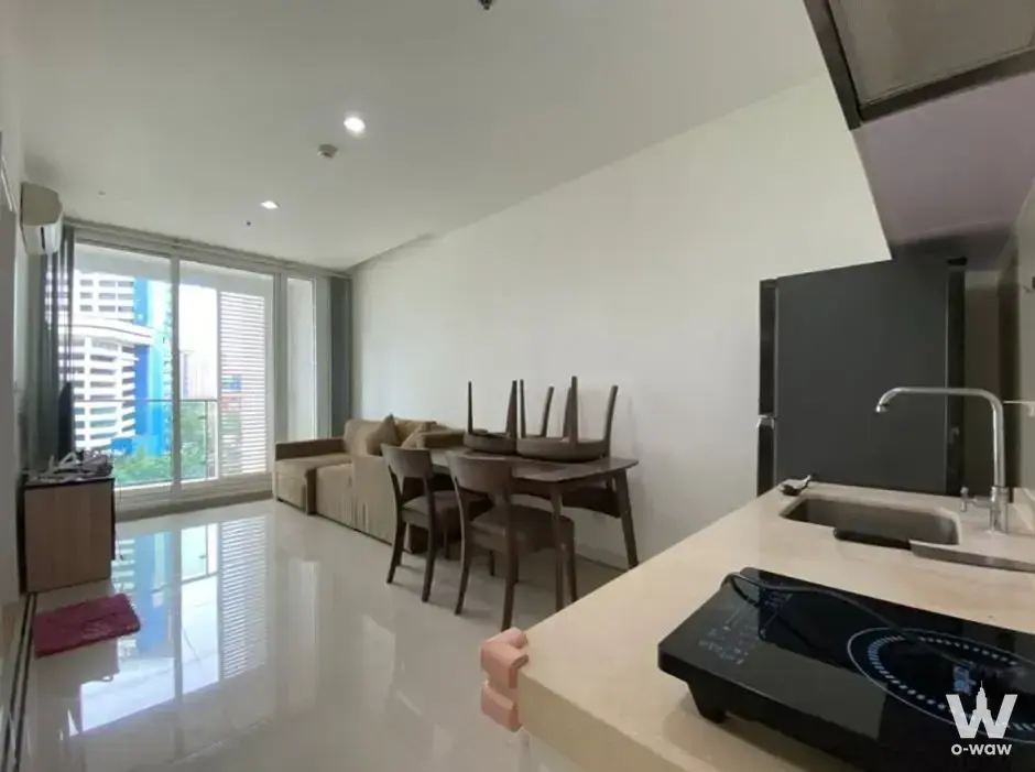 TC Green Rama 9 1-bed condo for rent with open-plan layout, beige L-shaped sofa, dining table, and city view from the balcony