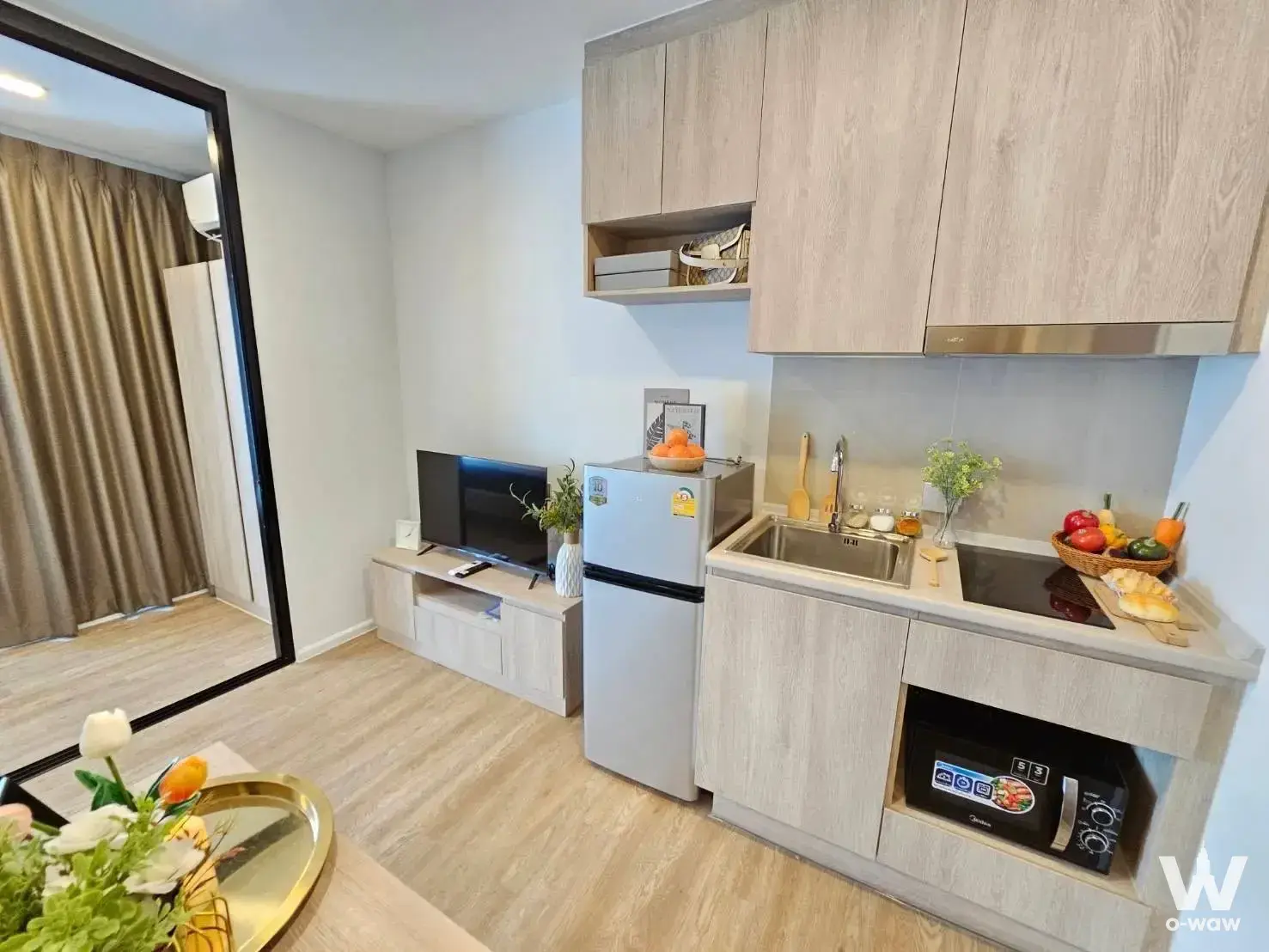 Modiz Sukhumvit 50 studio kitchenette with oak cabinets, induction cooktop, and large floor-to-ceiling mirror