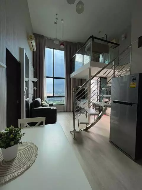 Loft-style living area in The Sky Sukhumvit condo with mezzanine, curved staircase, and city skyline view