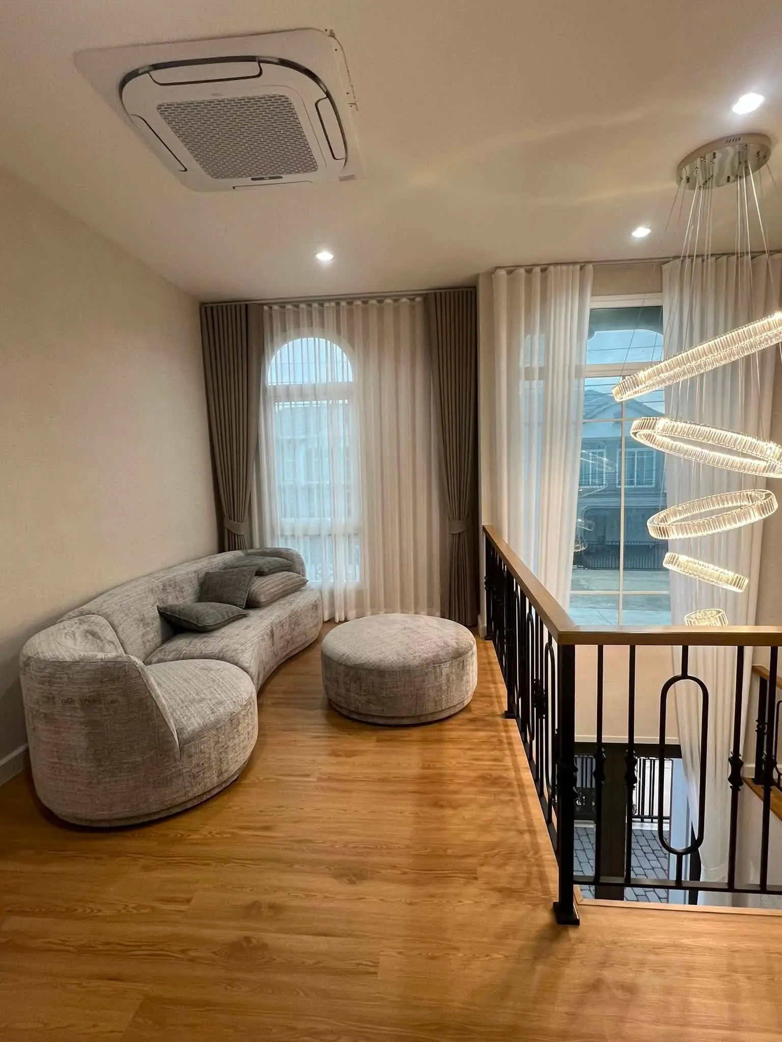 Upper-level living area featuring a curved grey sofa and crystal chandelier in this Grandio Bangna house