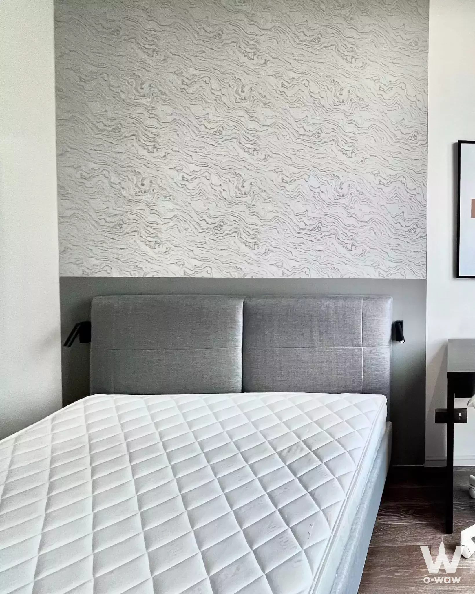 Minimalist bedroom with a grey upholstered headboard, charcoal accent wall, and topographic wallpaper in MUNIQ Sukhumvit 23