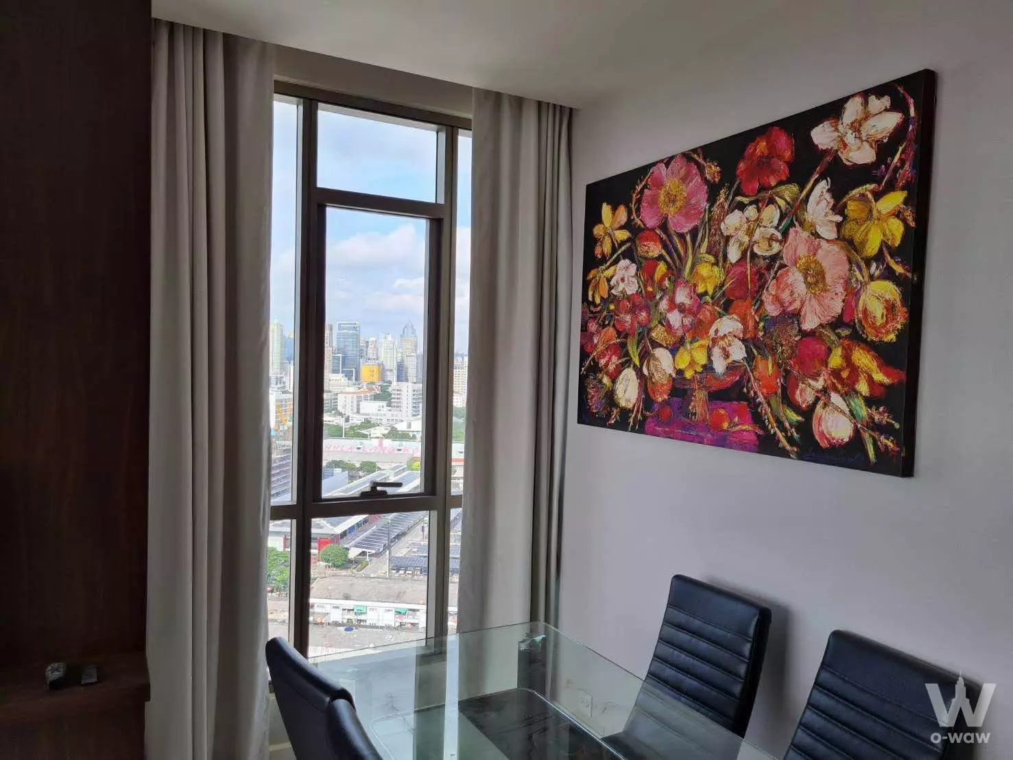Dining area in The Room Rama 4 2-bed condo with glass table, floral art, and floor-to-ceiling city views