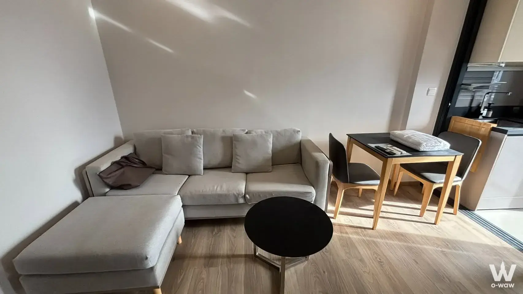 Open-plan living room in Oka Haus 1-bed condo featuring grey sectional sofa and dining set