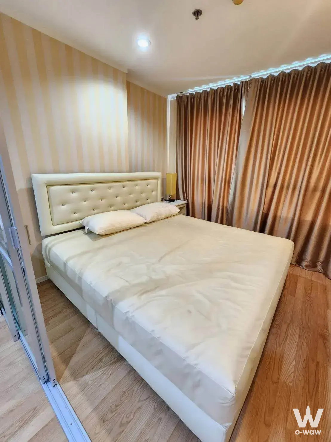 Lumpini Ville Naklua bedroom with tufted headboard, beige striped wallpaper, and bronze curtains