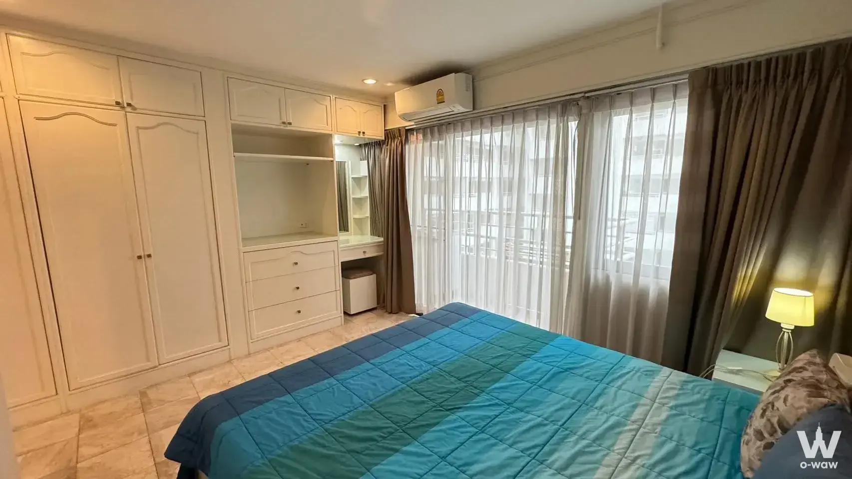 Furnished bedroom with blue striped comforter and white wardrobe in Saranjai Mansion condo