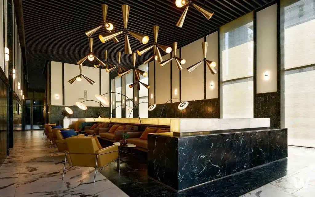 Luxury lobby lounge at Noble Form Thonglor with brass chandeliers and leather seating under a wood slat ceiling