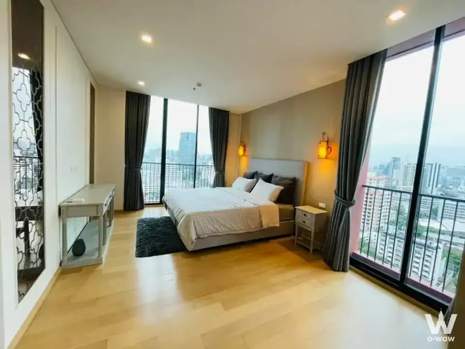 Master bedroom in Noble RE:D with grey upholstered bed and floor-to-ceiling balcony doors