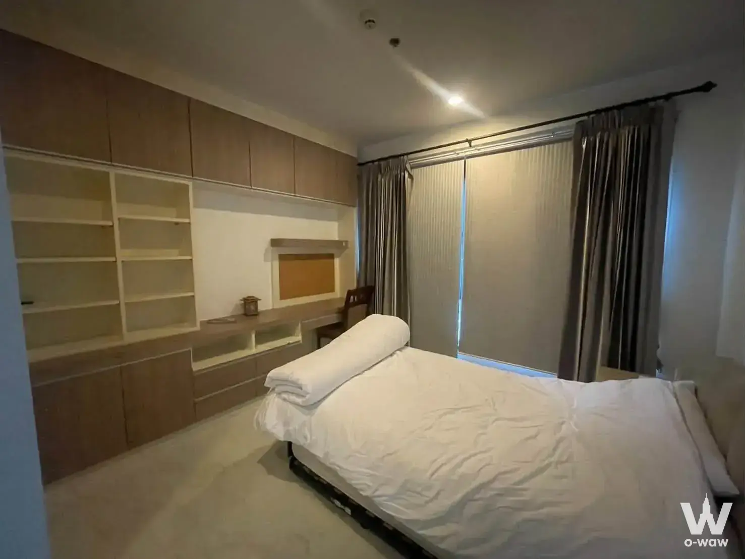 Spacious bedroom in The Vertical Aree with built-in light wood cabinetry and a full-length window