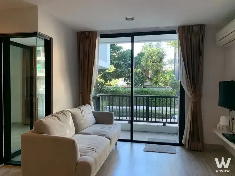 Beige sofa and TV in a D65 Condominium living room with balcony access and lush green views