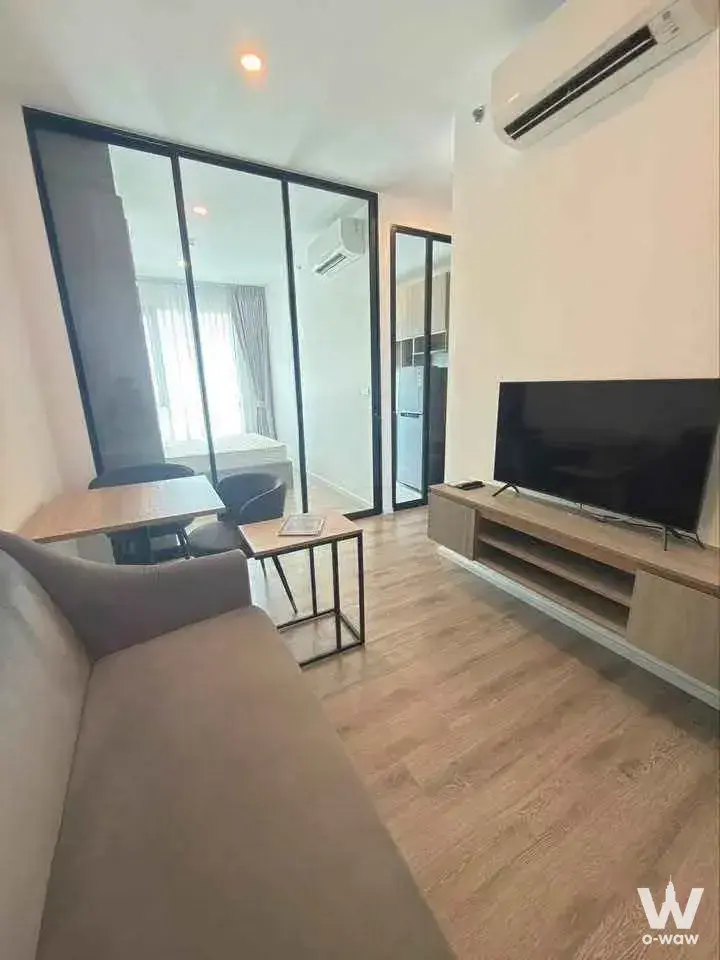 Living room in Knightsbridge Sukhumvit-Thepharak with grey sofa, wood console, and glass partition to bedroom