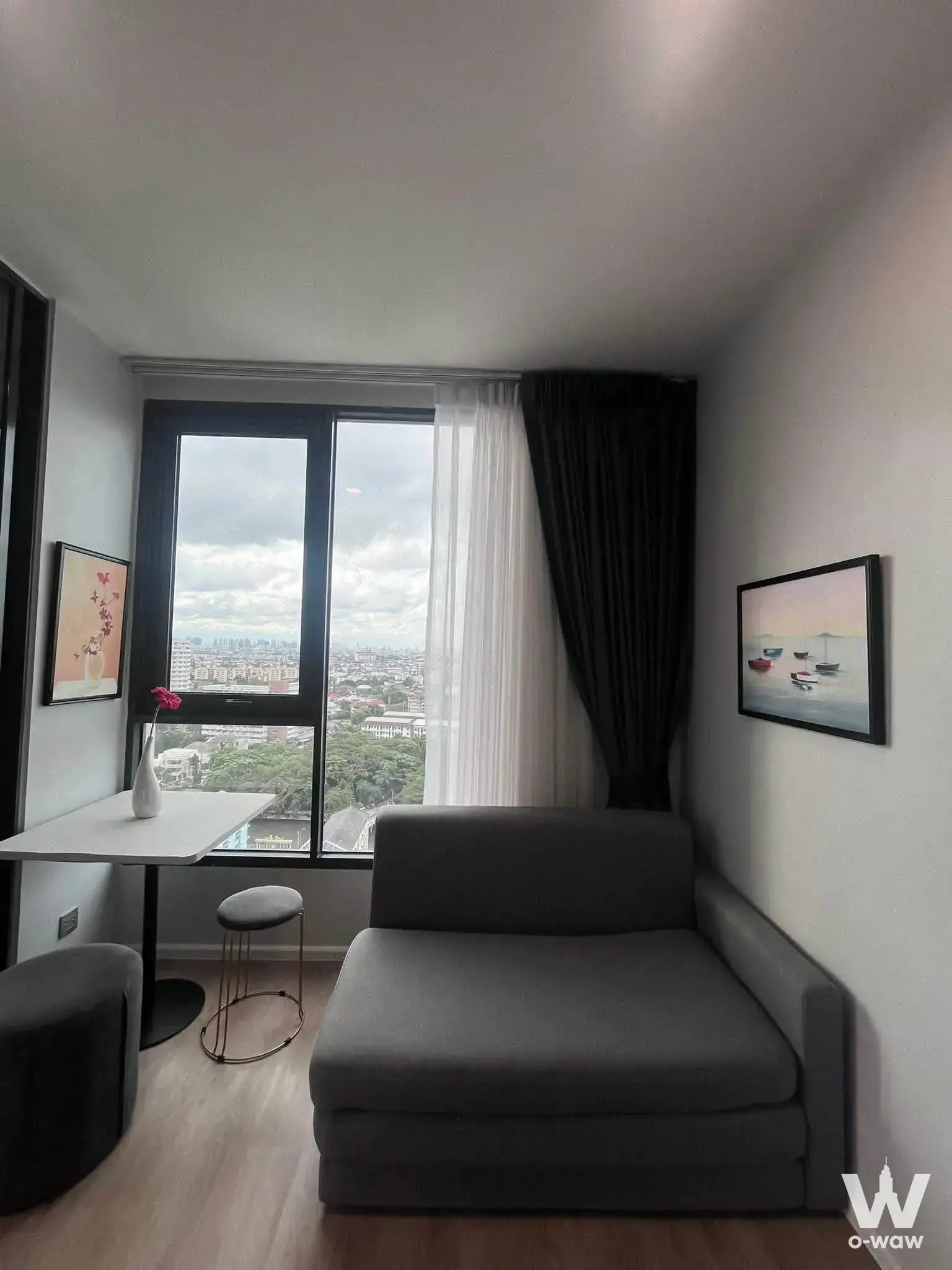 Small living area in a 1-bed Modiz Rhythm Ramkhamhaeng condo with a high-floor city view and grey chaise lounge