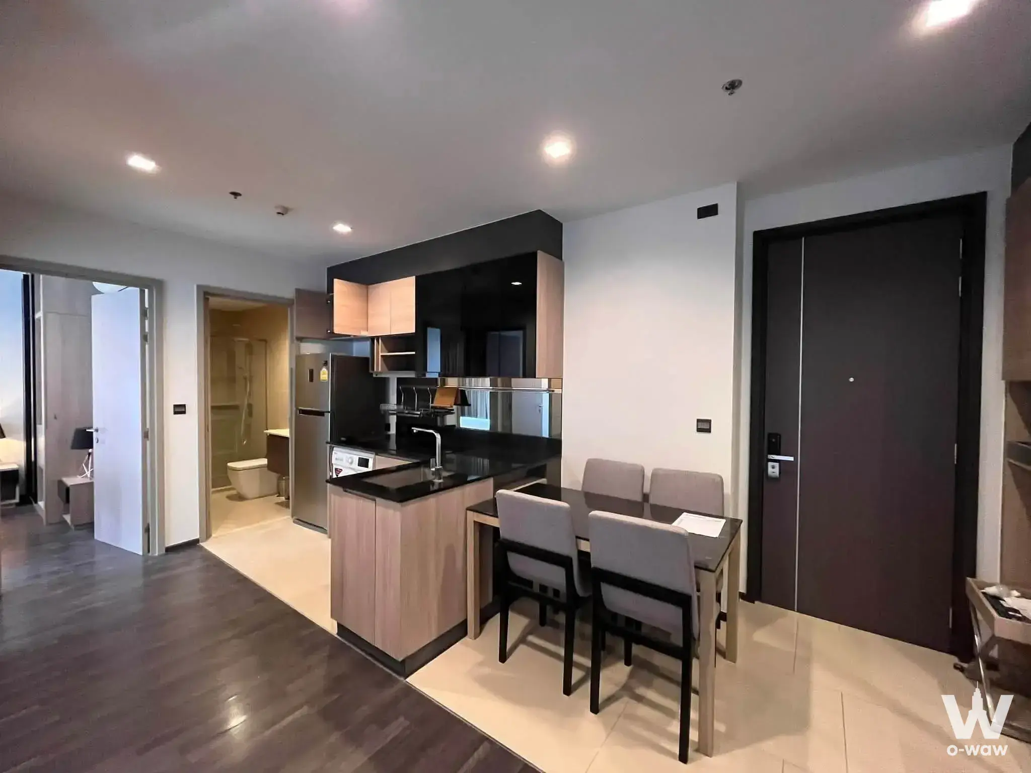 Open-plan living area with black granite island and dining set in a 2-bed condo at THE LINE Asoke-Ratchada