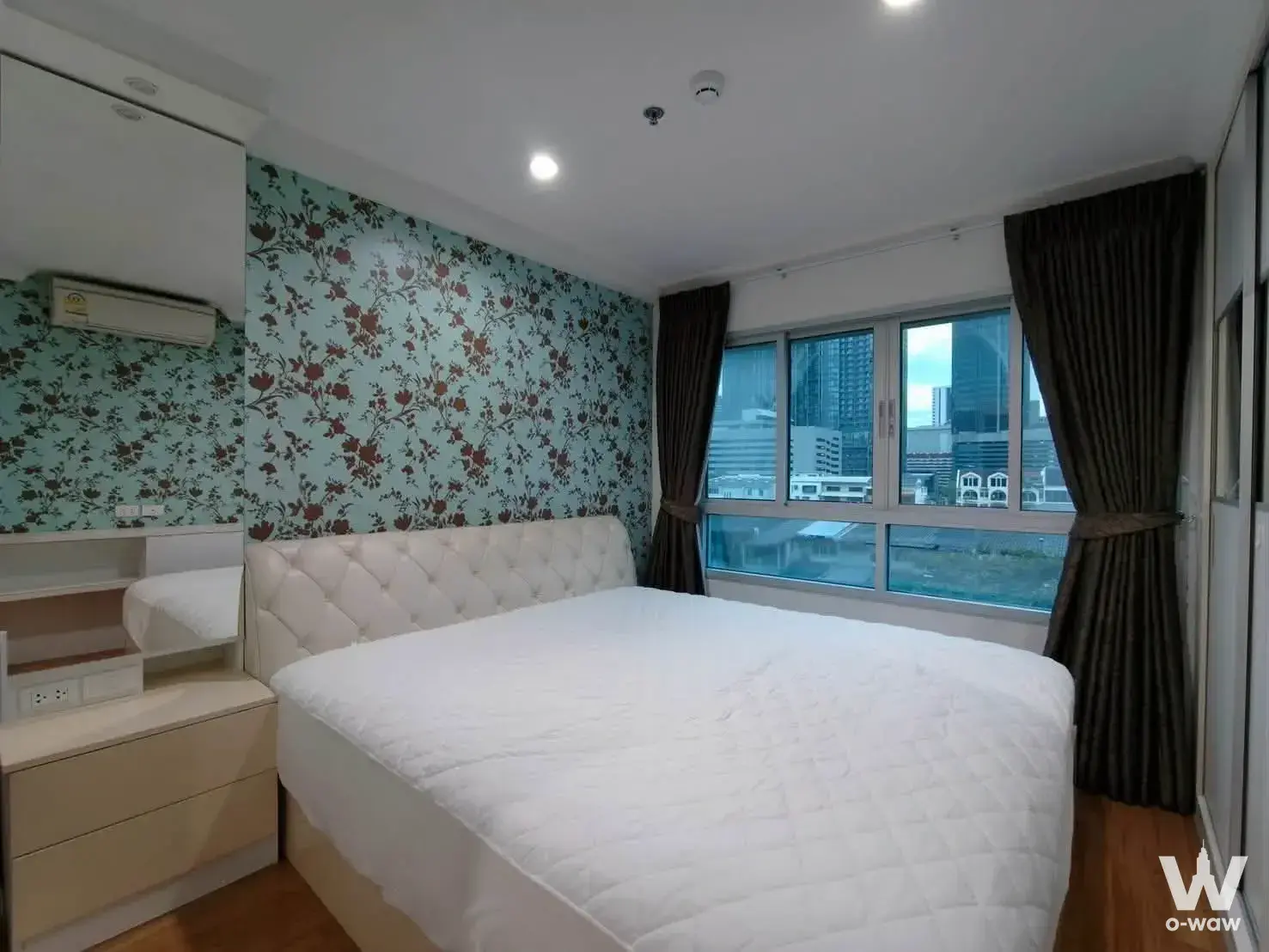 Bedroom in a Lumpini Place Rama 9 condo with queen bed and mint-green floral accent wallpaper