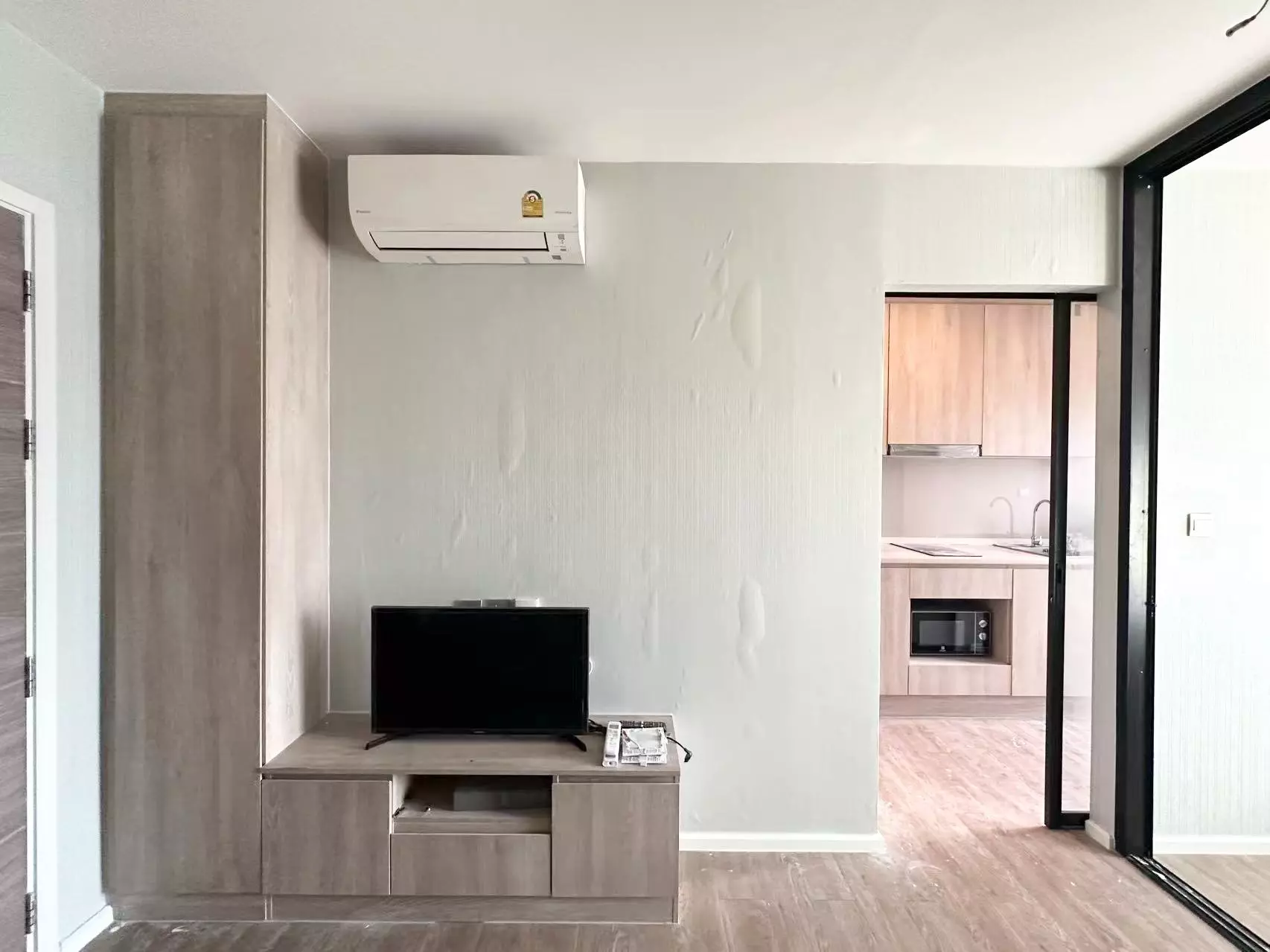 Modiz Sukhumvit 50 living room featuring grey wood-look floors, tall built-in cabinet, and open kitchen view
