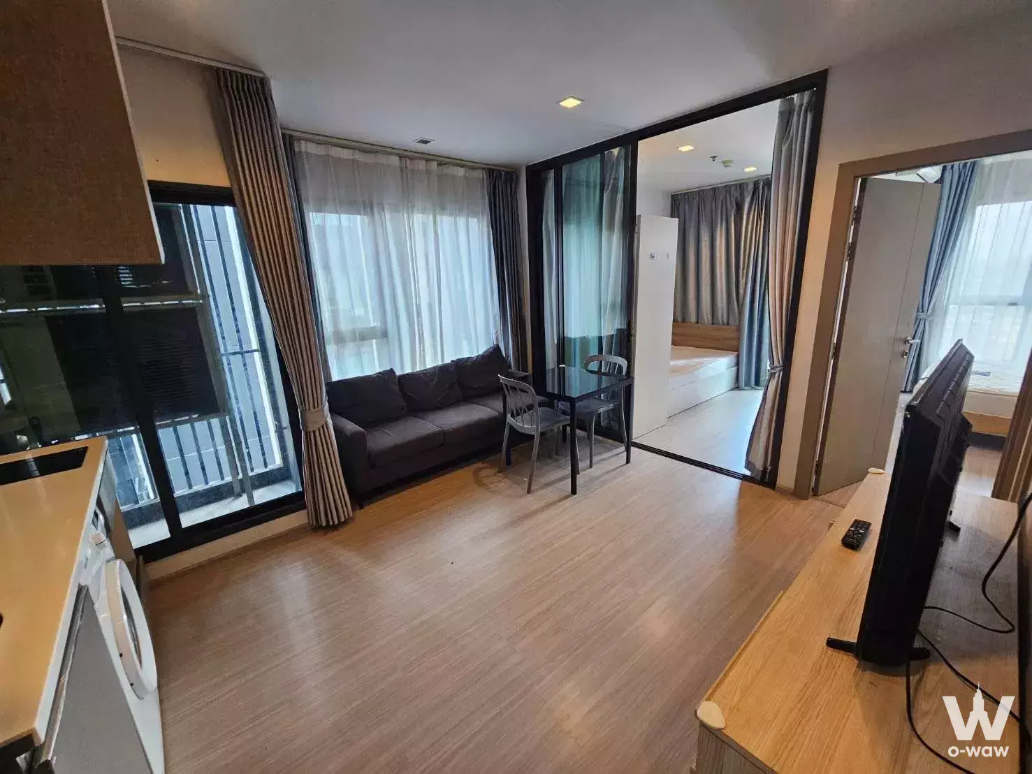 Modern 2-bed condo living area in Life Asoke - Rama 9 featuring dark grey sofa, glass partition, and neutral tones