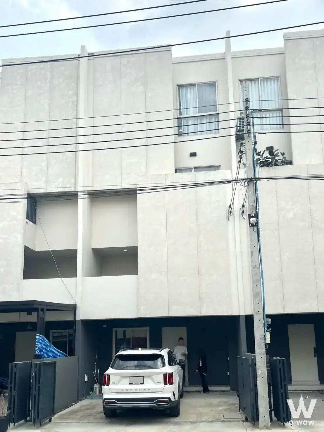 This 3-bed townhouse for rent at Nue Verse Krungthep Kreetha has a modern facade, balconies and a carport with a white SUV