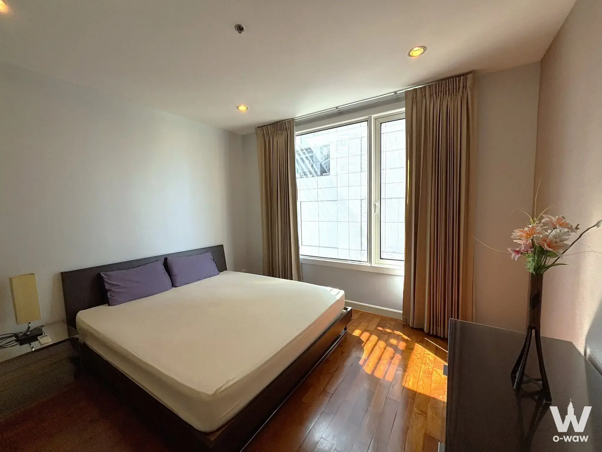 Bedroom in a Siri Residence condo with queen bed, purple pillows, and hardwood floors