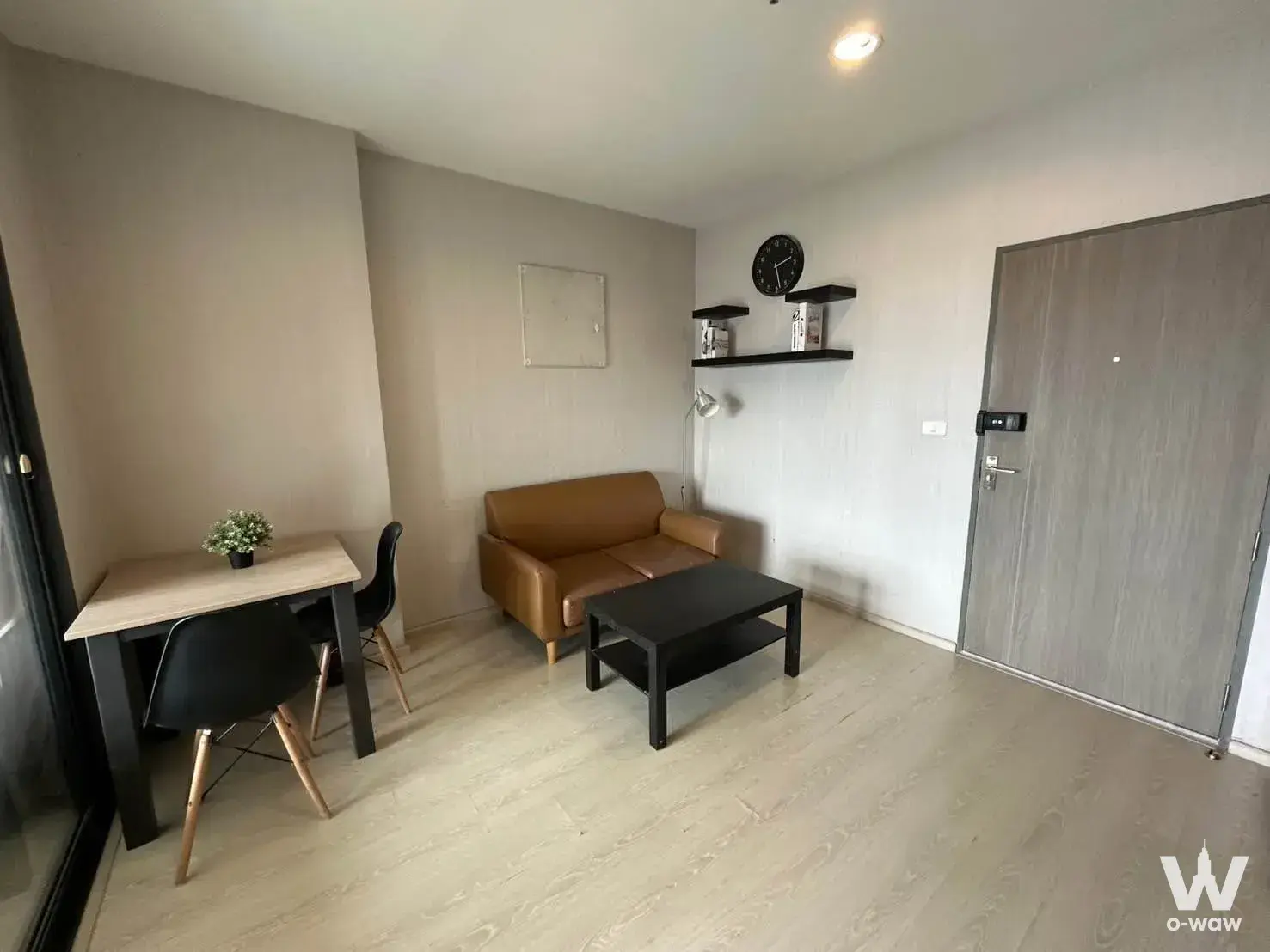 Studio living area in an IDEO Sukhumvit 115 rental showcasing caramel leather sofa, light wood dining set, and minimalist