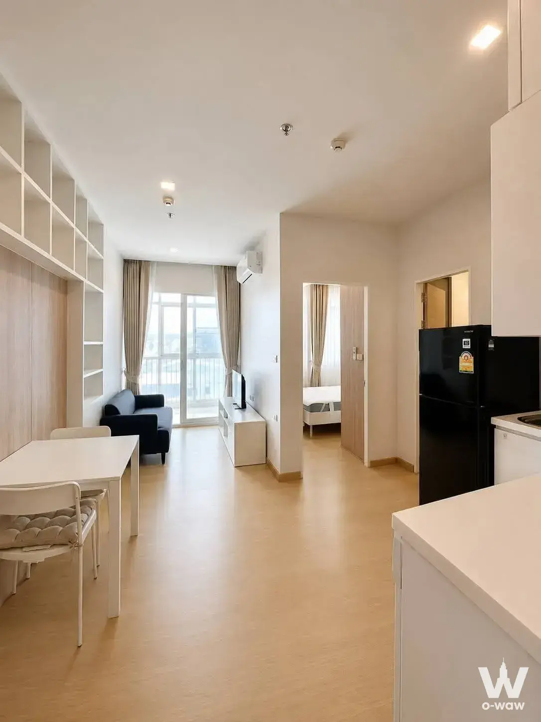 Open-plan living area with grey sofa and balcony access in a 1-bed condo for rent at The Coast Bangkok