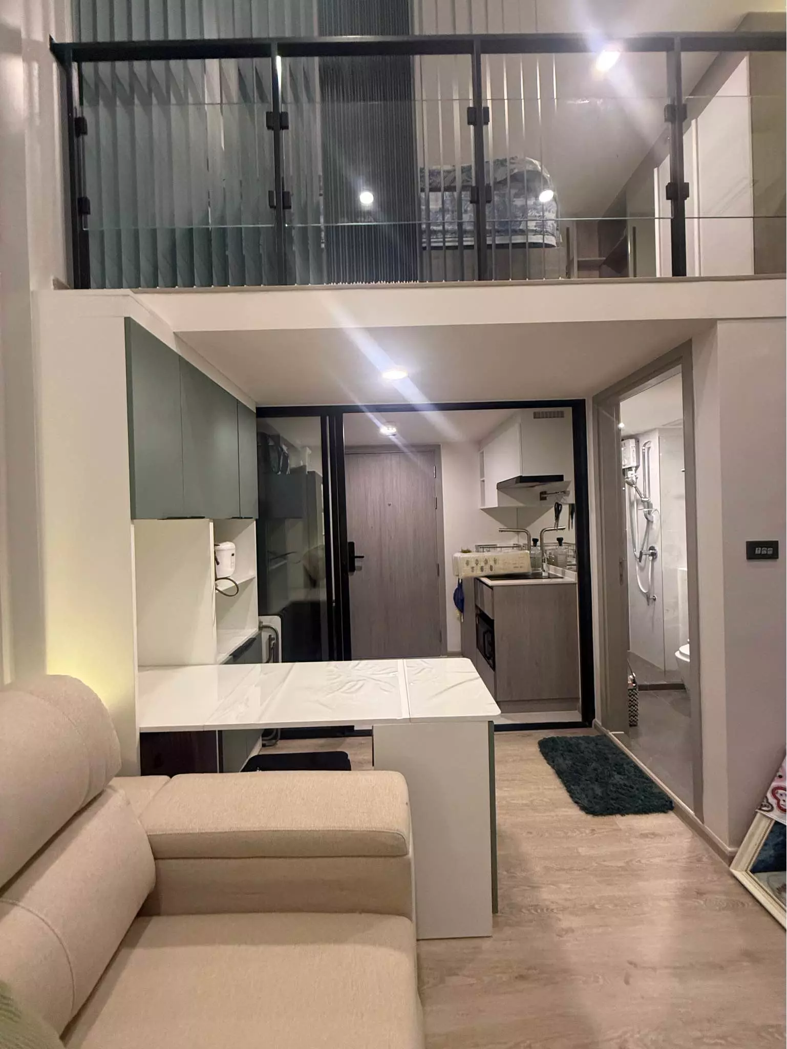 Mezzanine loft layout with a sage-green kitchenette and glass railing in this 1-bed condo for rent at Origin Plug & Play