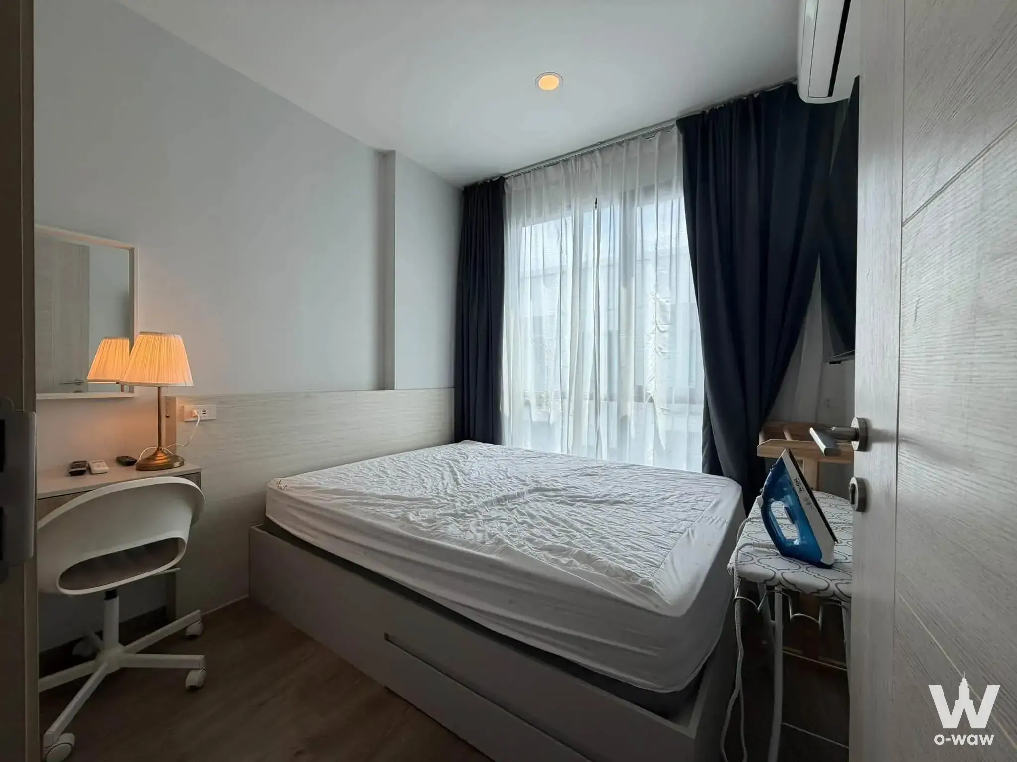 The compact bedroom in a Brompton Pet Friendly Samrong Station 1-bed rental has a storage bed, desk and ironing board