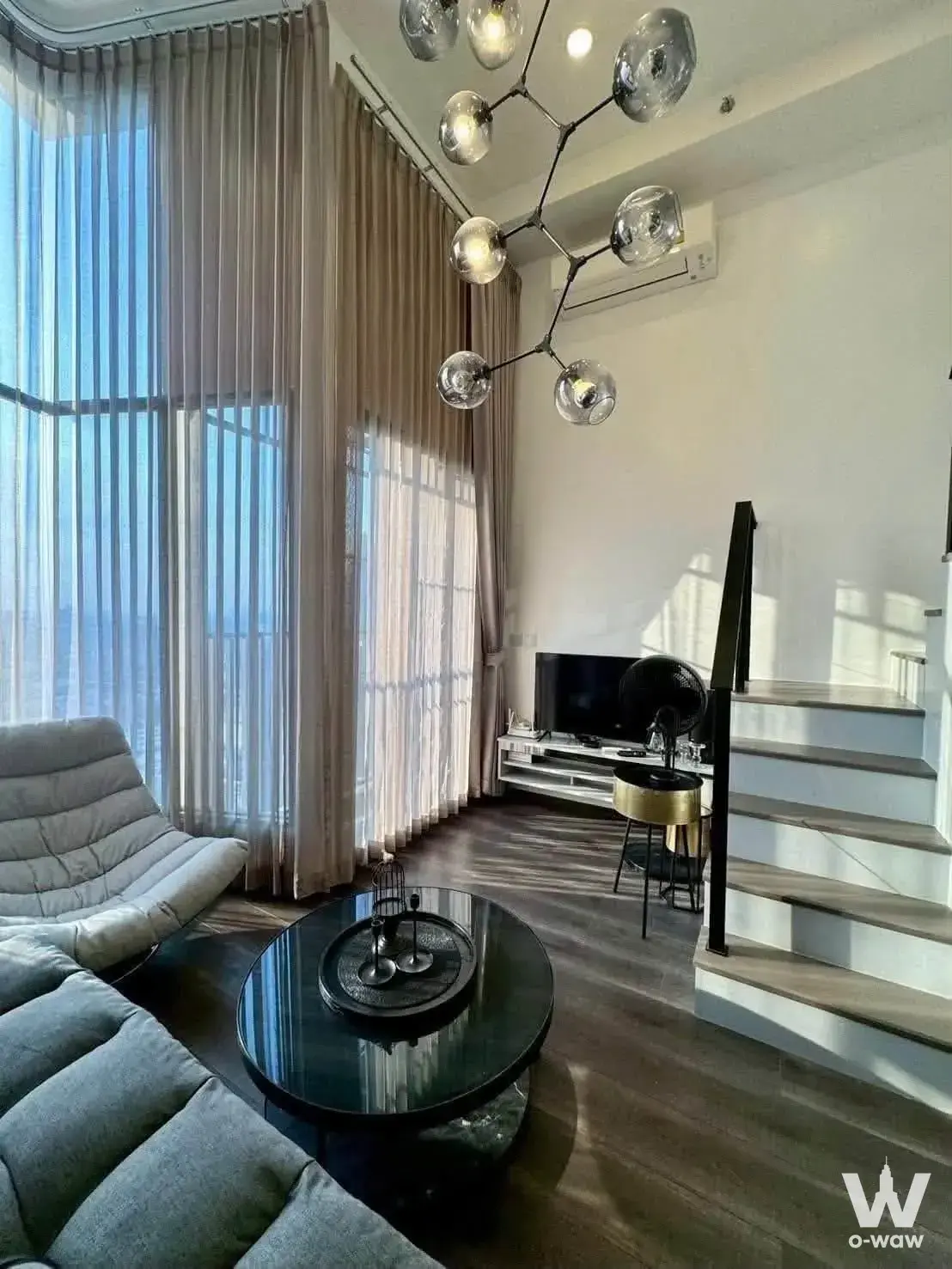 Modern loft living room with grey sectional sofa, black glass coffee table, and sputnik chandelier in KnightsBridge Space