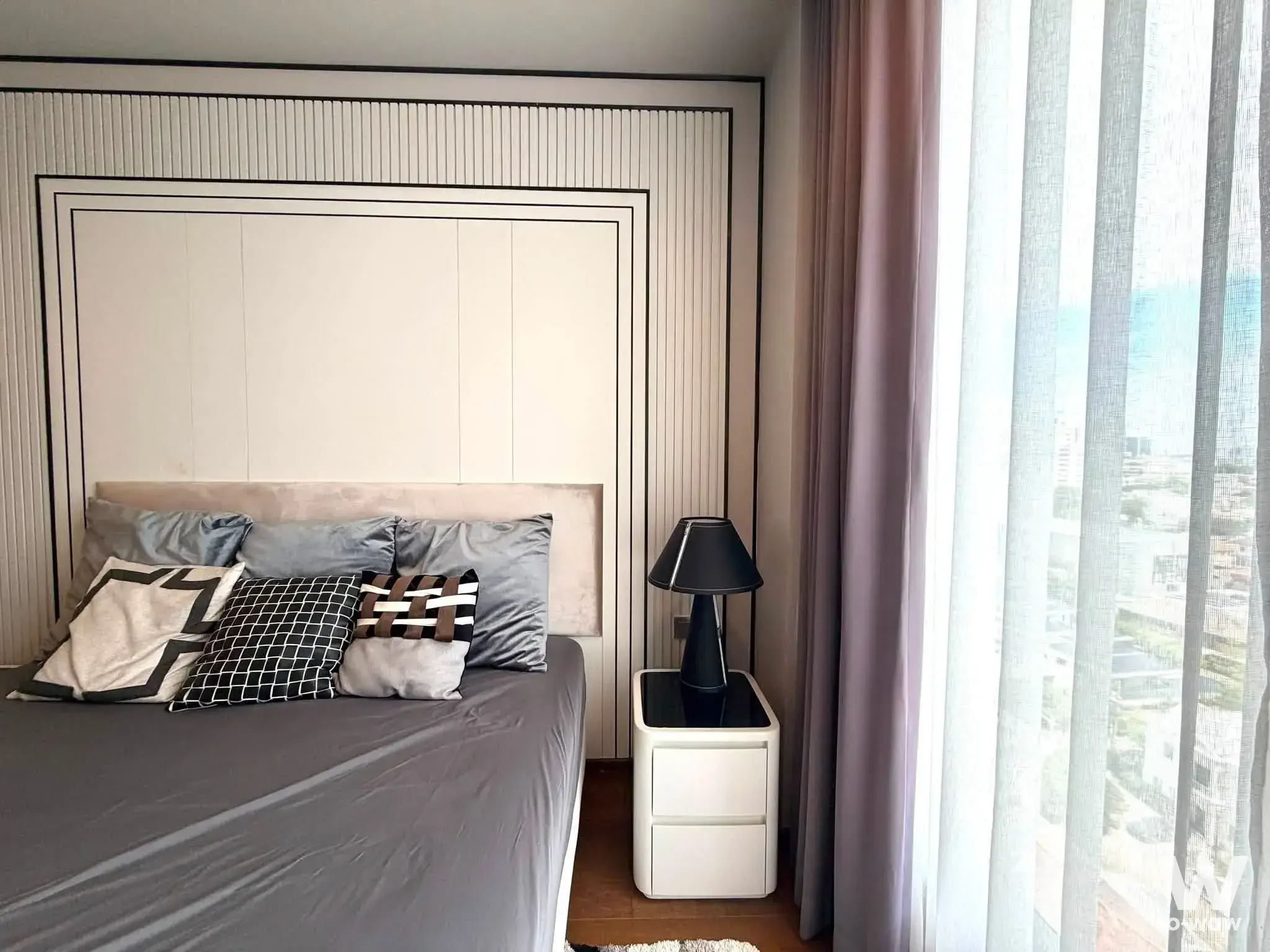 Staged bedroom in Ideo Q Sukhumvit 36 condo with fluted paneling, city view, and neutral decor