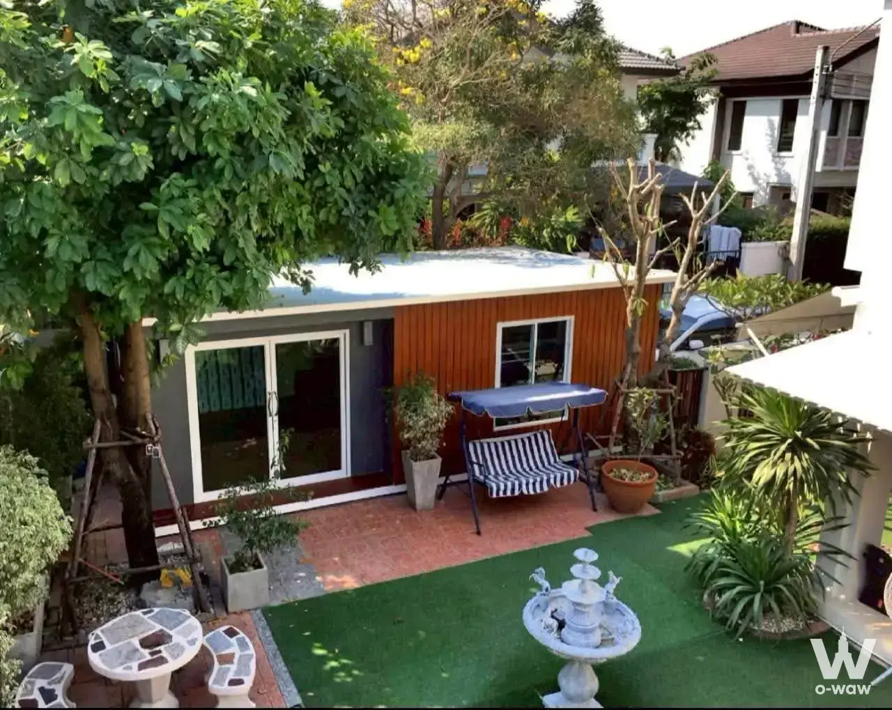 Garden cottage with orange wood slats and brick patio featuring a swing bench and fountain